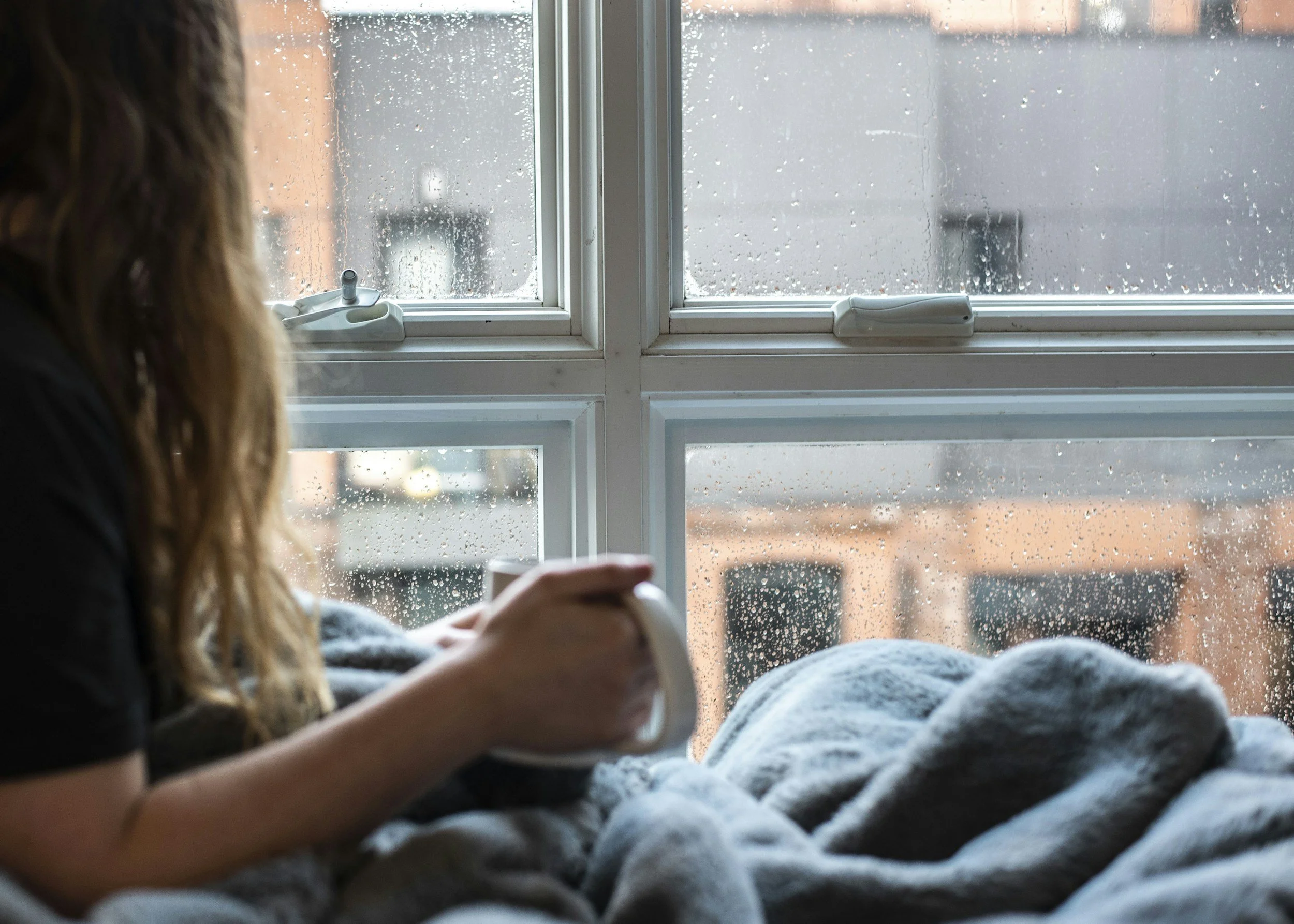 Person sitting by a window with a cup of coffee, looking thoughtful on a quiet evening