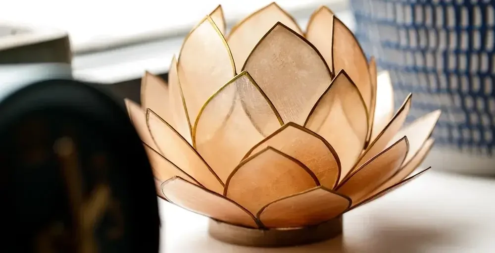 A decorative lamp shaped like a lotus flower with beige and gold-colored petals, placed on a surface with a blurred background.