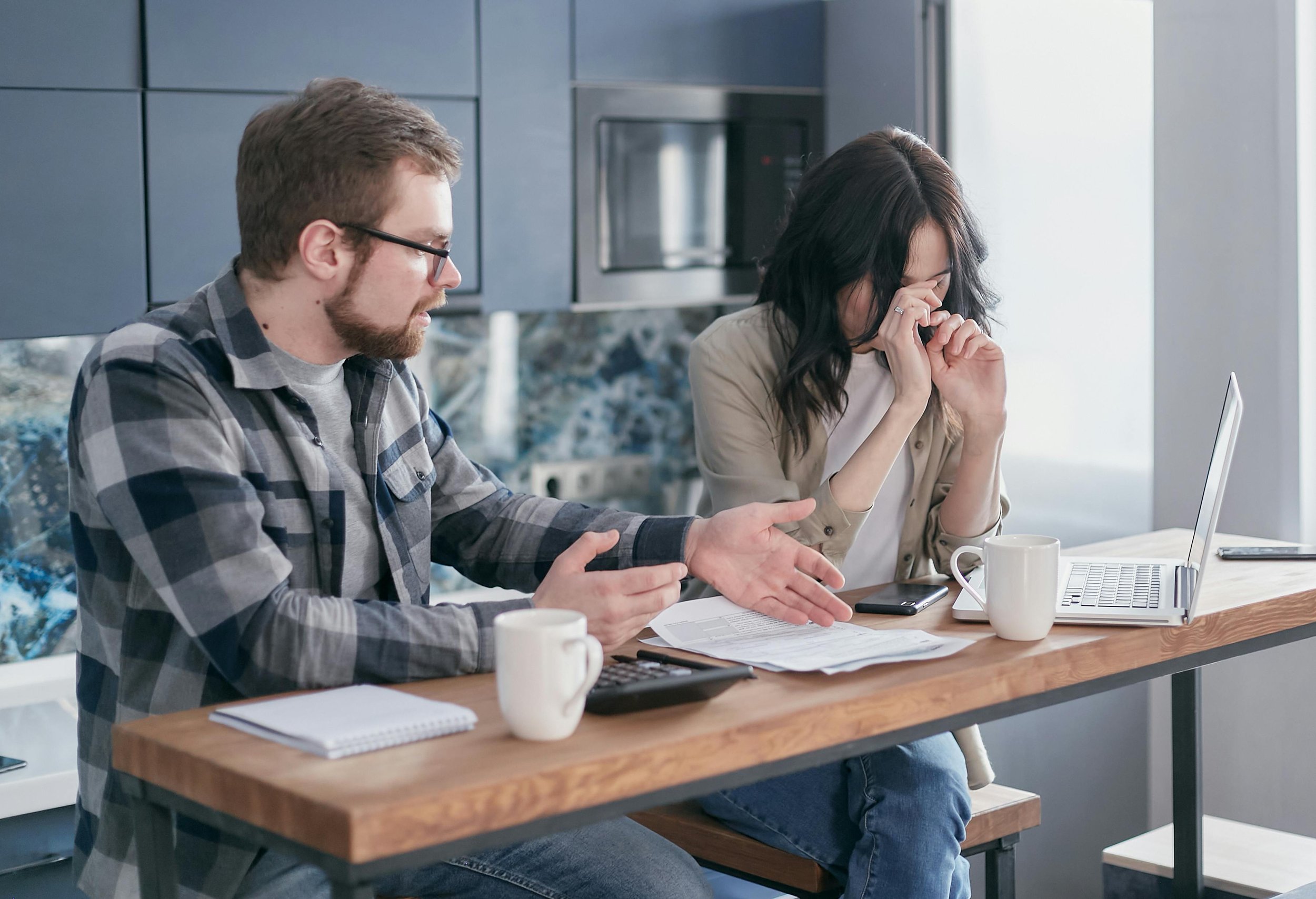 Engaged couple feeling stressed while reviewing wedding expenses and travel details on a laptop at home.
