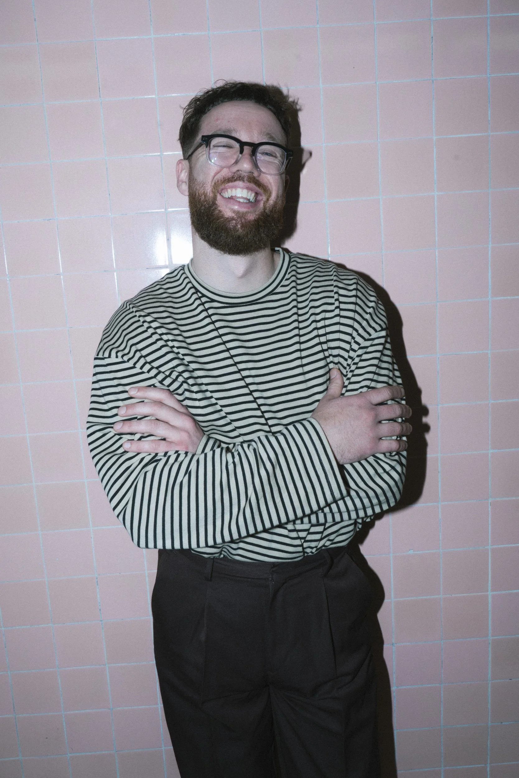 Musician laughing with arms crossed against pink tiled wall beneath Flinders Street Station, Melbourne