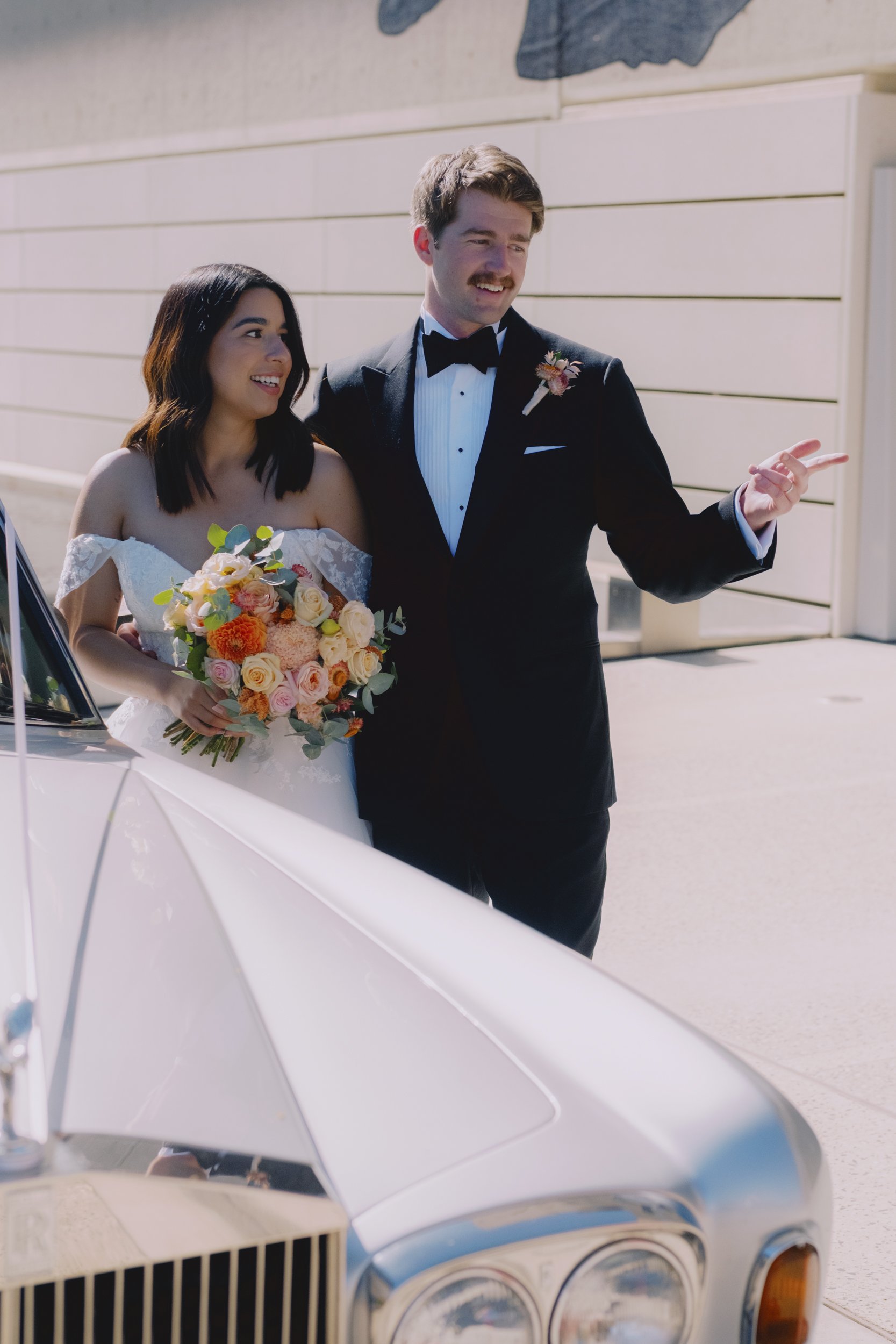 Bride and groom laughing beside a vintage Rolls-Royce outside the NGA, Canberra