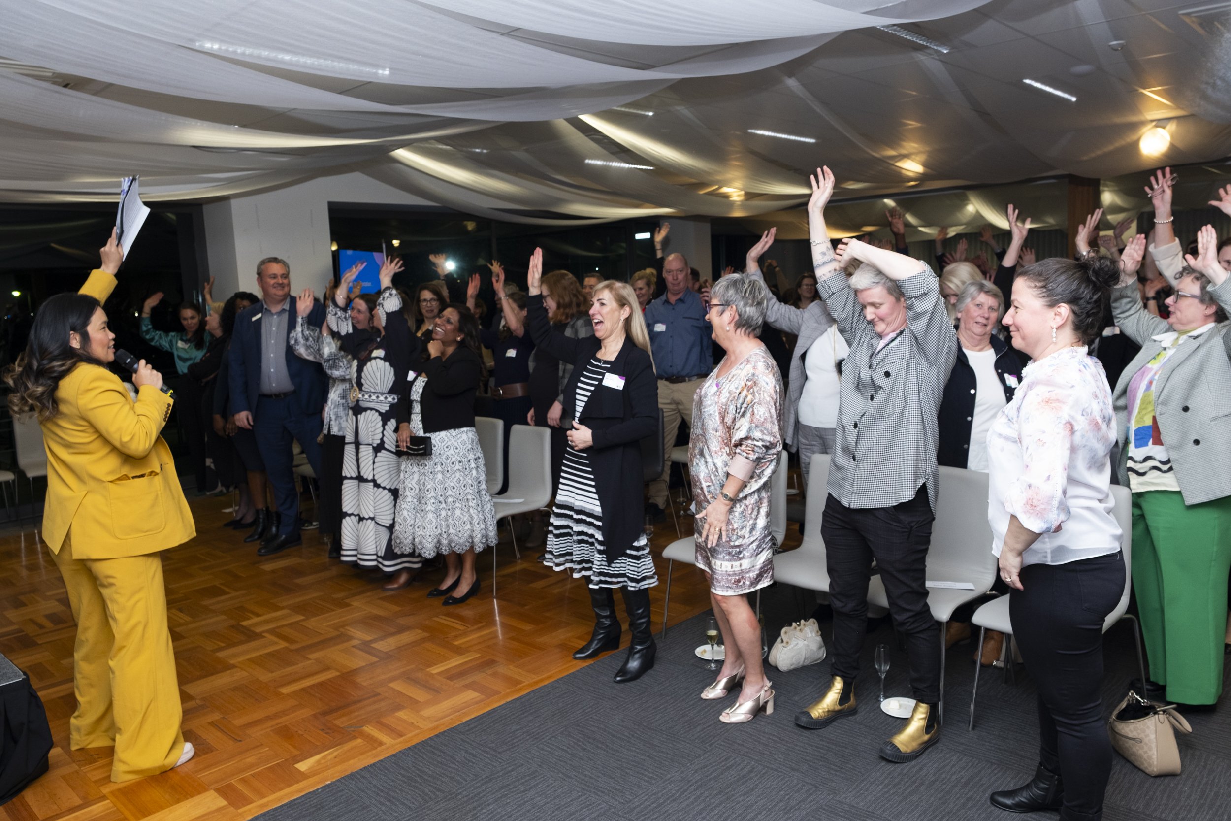 MC leading an energetic crowd participation moment at a Western Health Foundation corporate event, with guests raising their hands and laughing