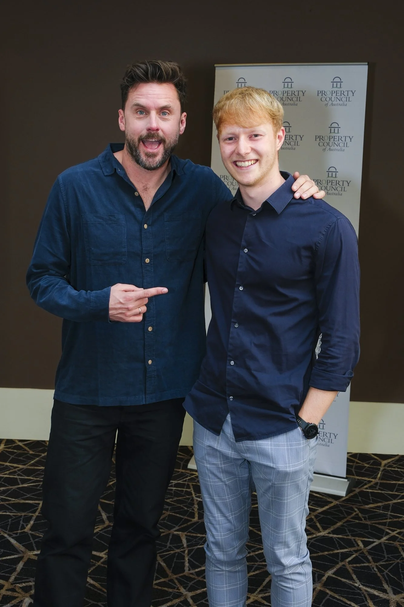 Dave Thornton posing with a guest in front of a Property Council of Australia media wall at the Hyatt Canberra
