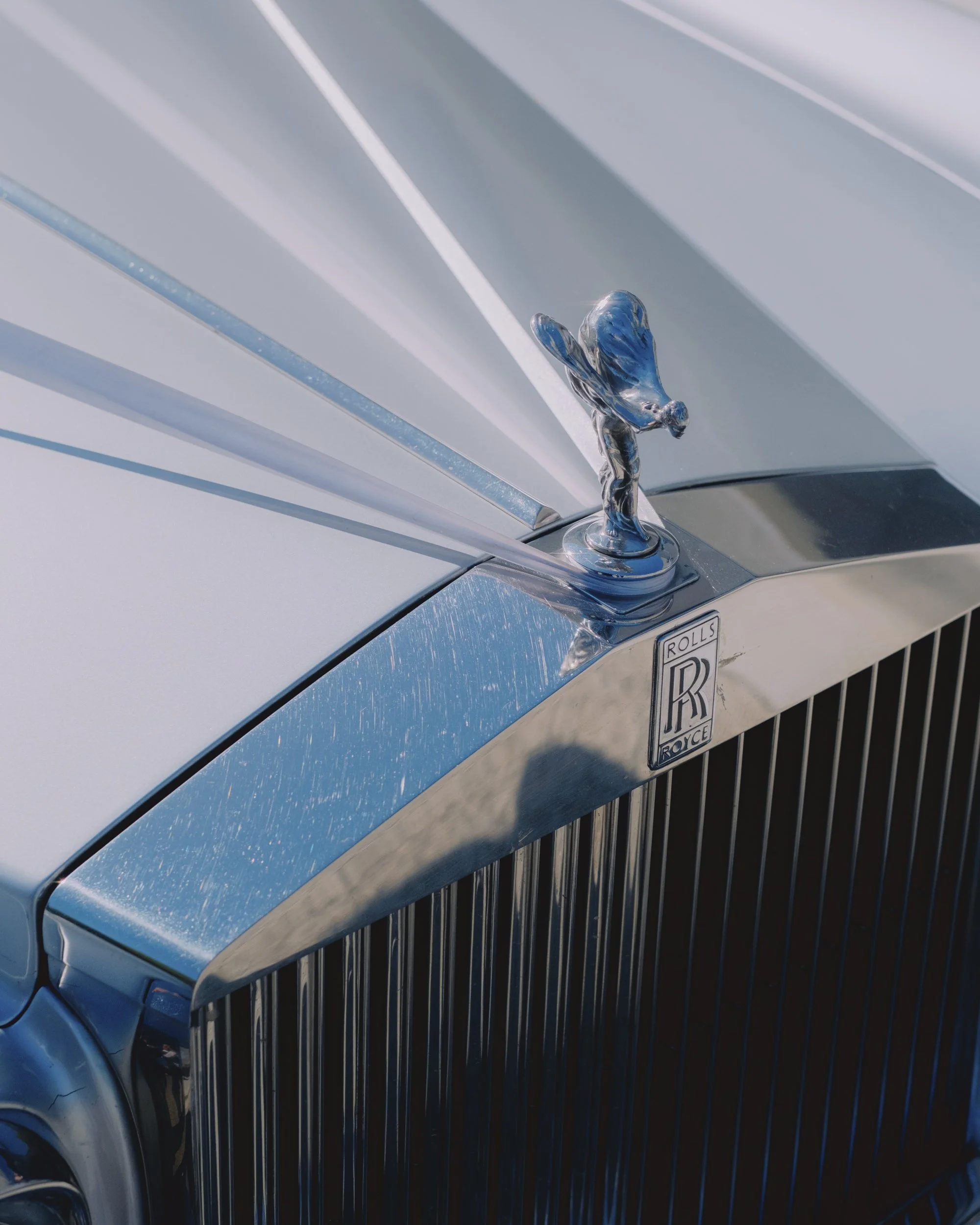 Close-up detail of the Spirit of Ecstasy hood ornament on a vintage Rolls-Royce wedding car, with ribbon streamers