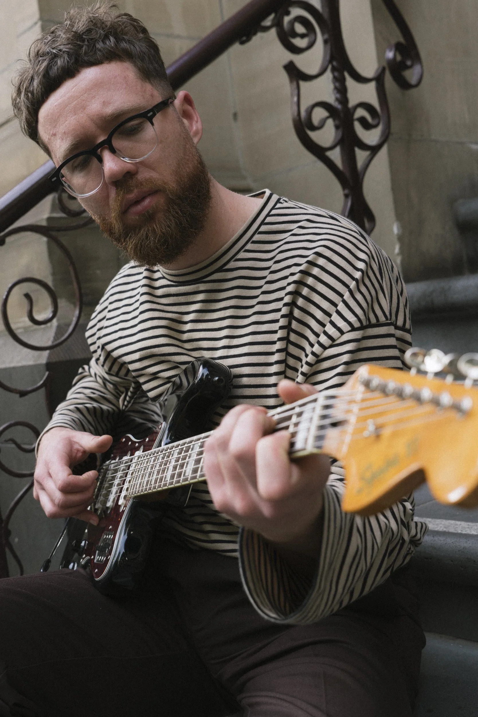 Close-up of musician playing Fender Jaguar guitar on stone steps, Melbourne CBD heritage building