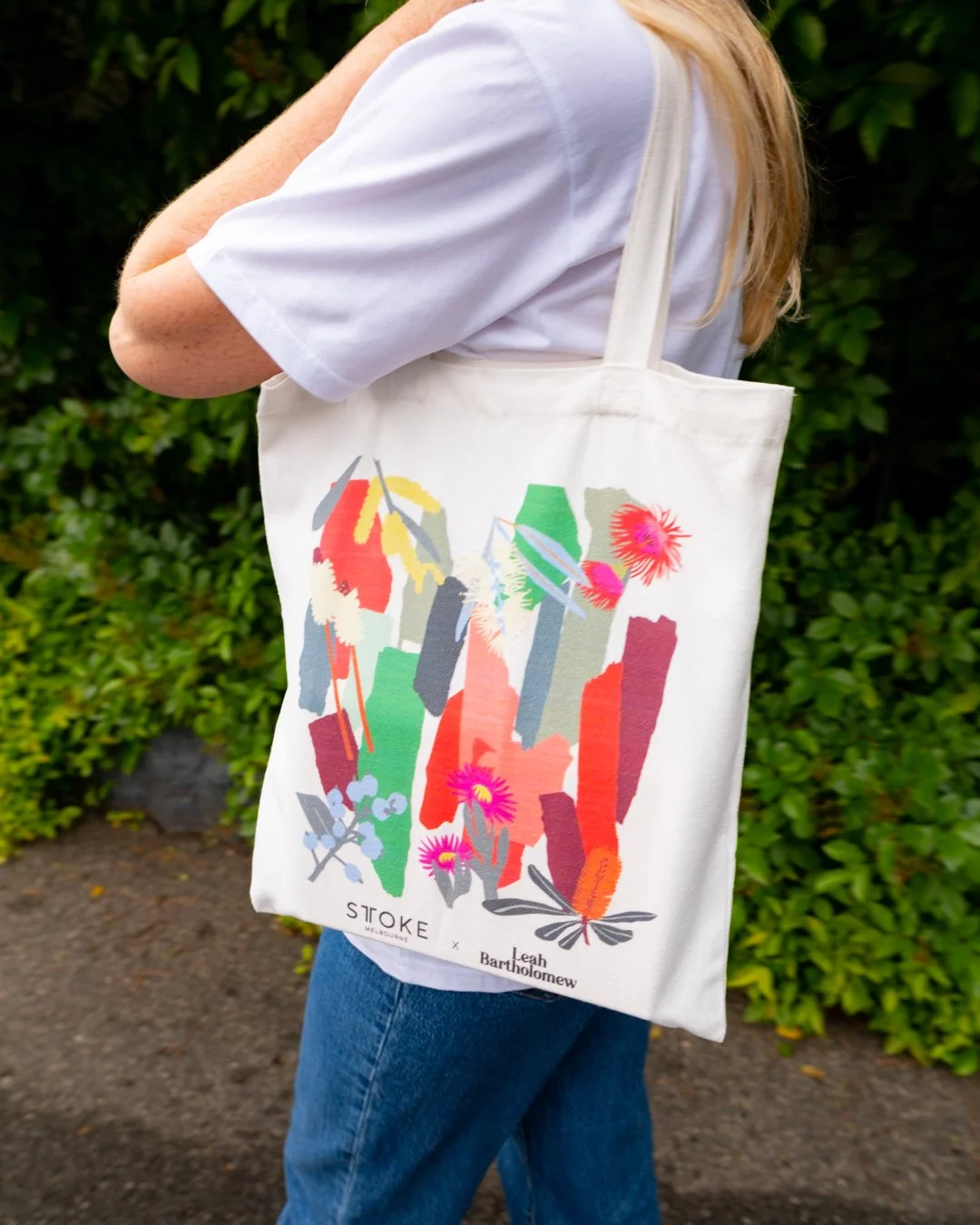 Leah Bartholomew carries the STTOKE x Leah Bartholomew tote bag over her shoulder while walking along a leafy outdoor path