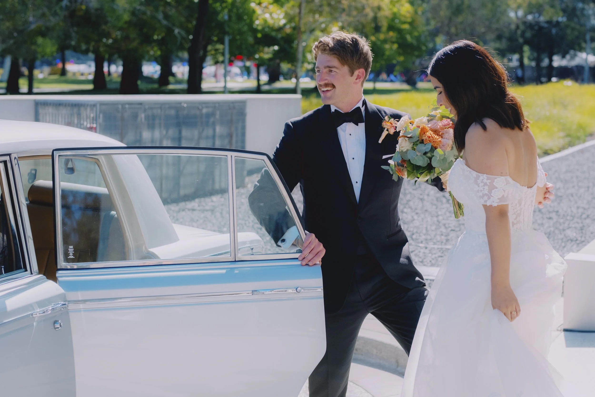 Bride and groom sharing a laugh beside the open door of a vintage Rolls-Royce, NGA precinct, Canberra