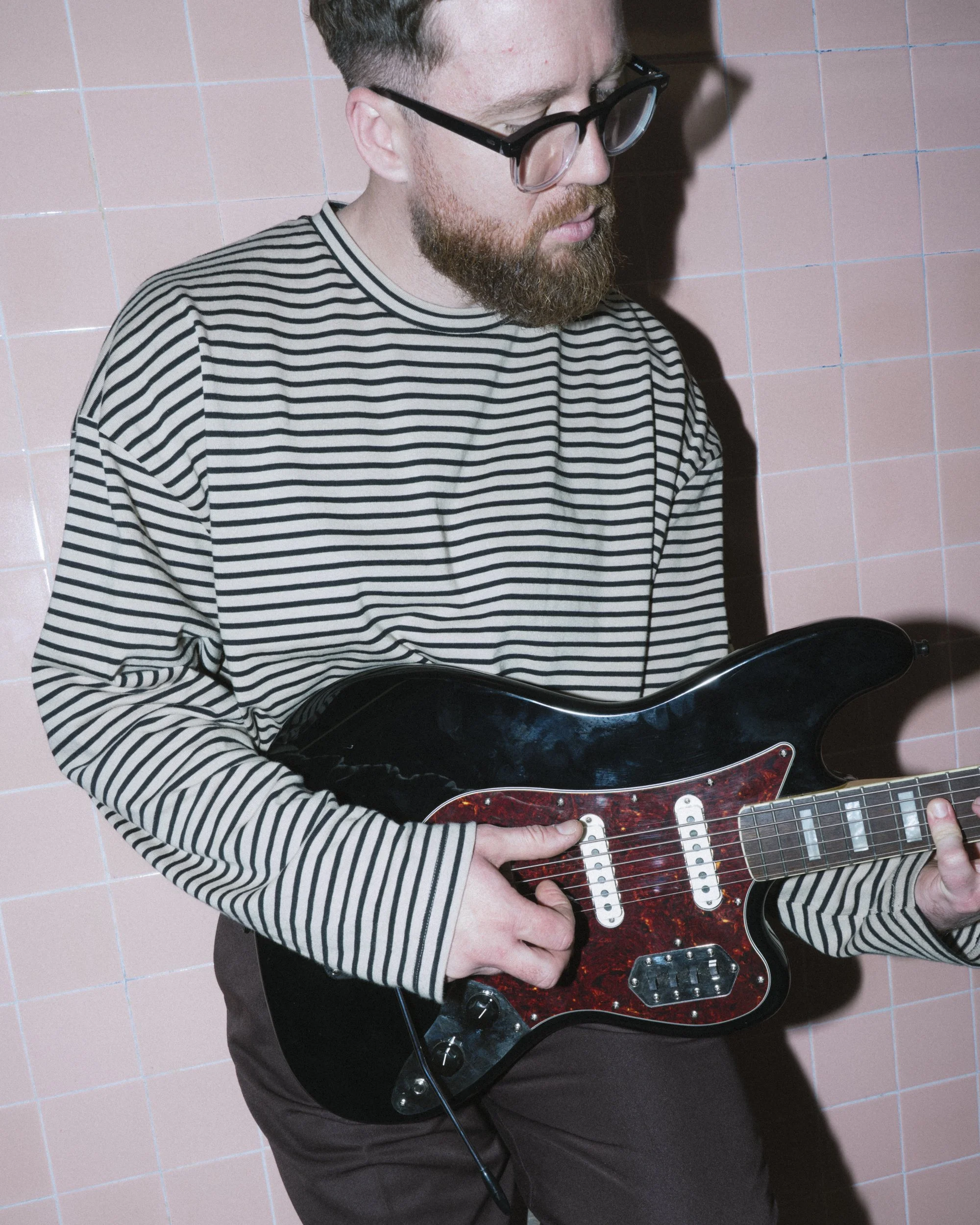 Musician playing electric guitar against pink tiled wall, Flinders Street Station underpass, Melbourne