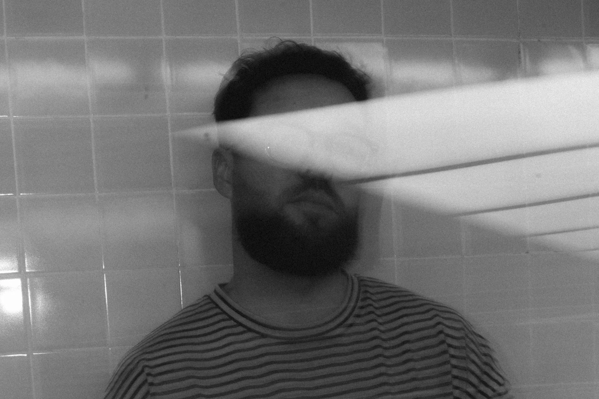 Black and white abstract double-exposure portrait with light streak obscuring face, tiled wall background