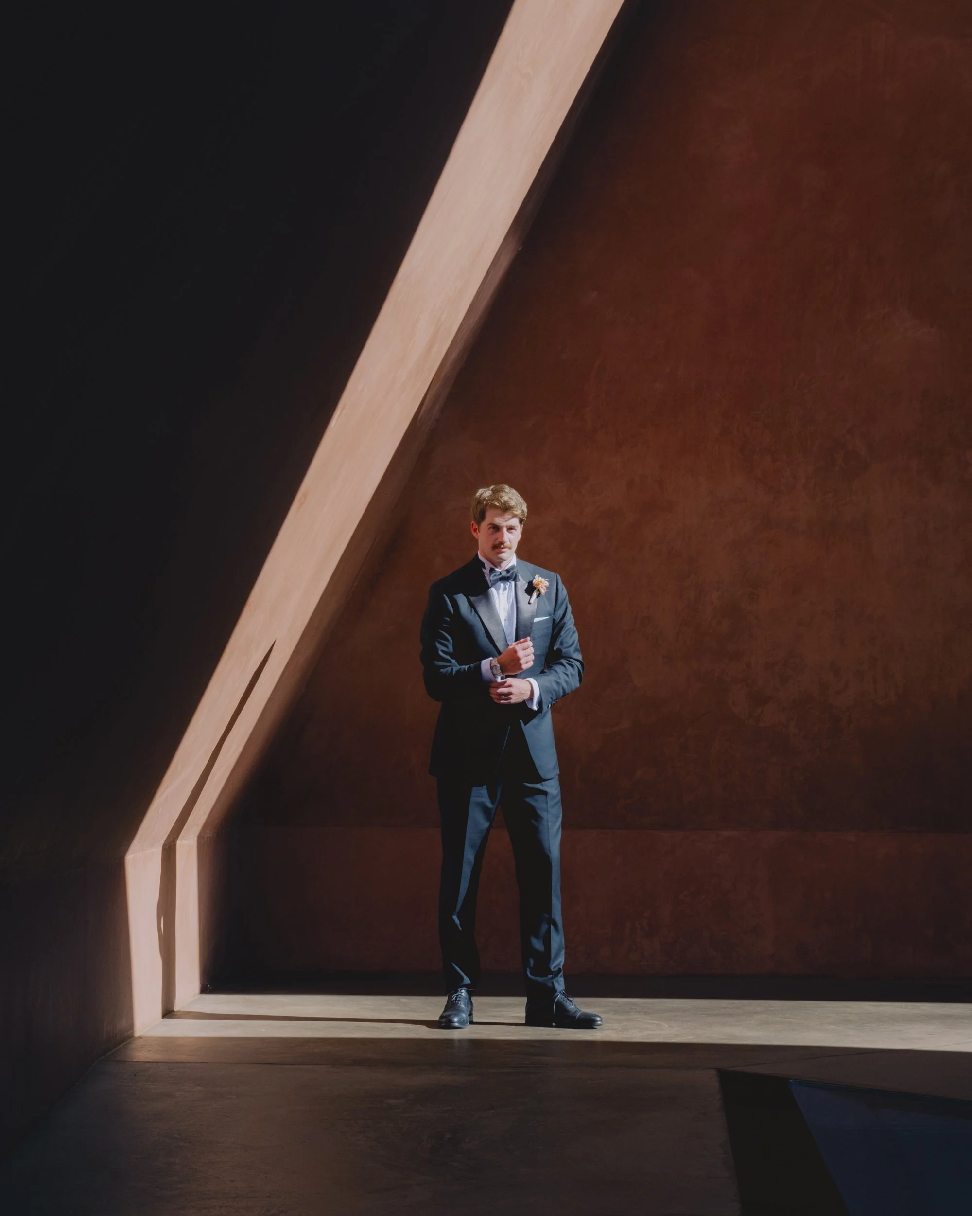 Groom portrait inside the James Turrell Skyspace near the NGA, Canberra, dramatic diagonal light cutting across terracotta walls