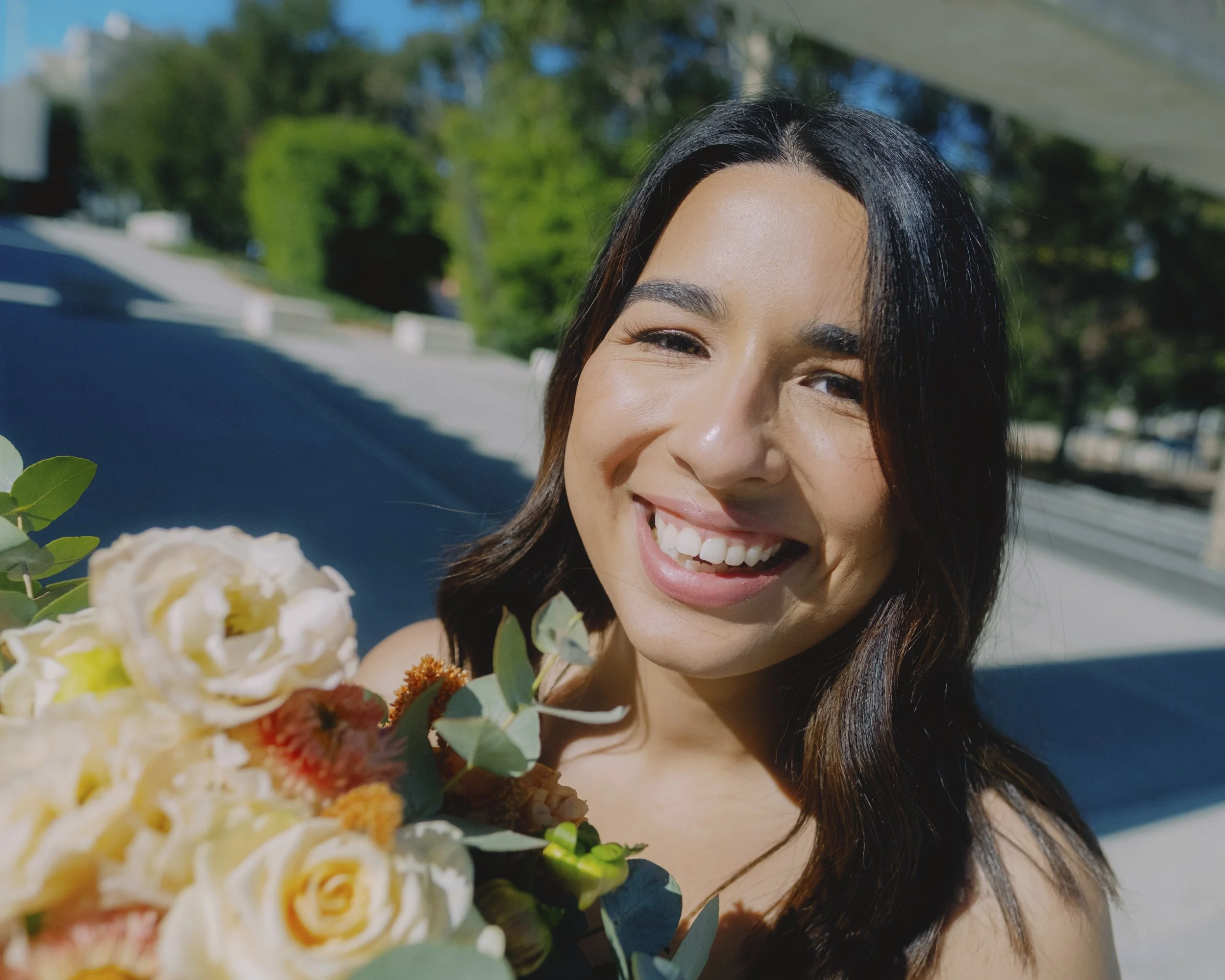 Close-up portrait of a smiling bride holding her bouquet in bright sunlight outside the National Gallery of Australia, Canberra