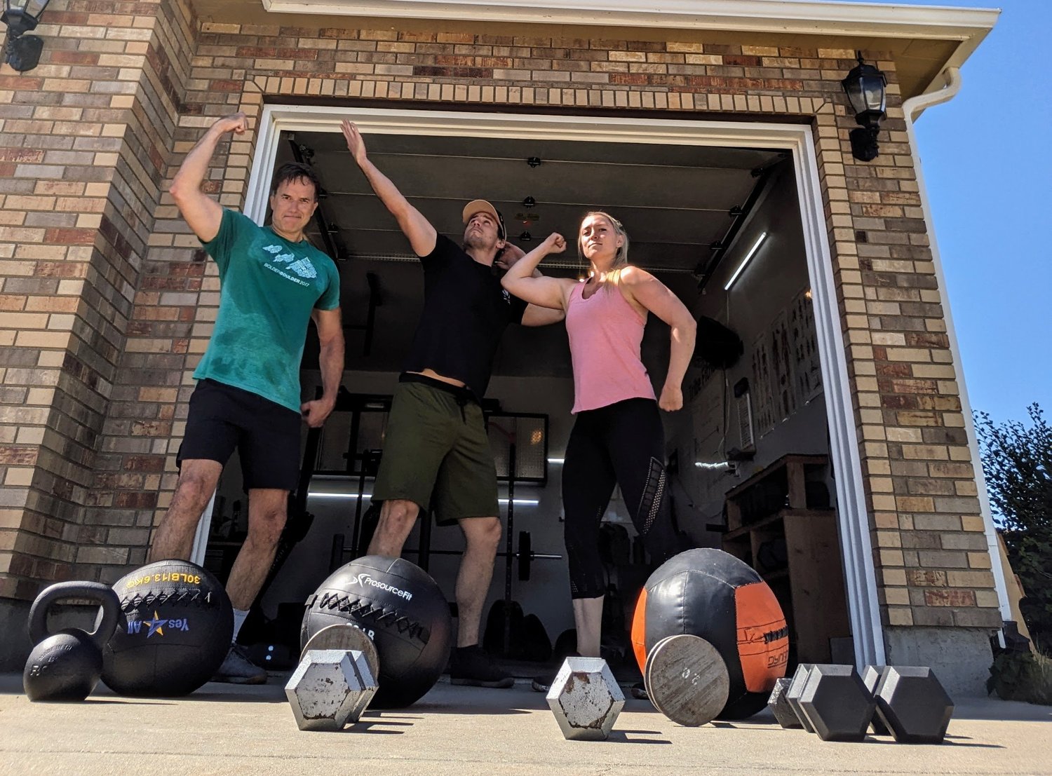 Sam Moses and two Tribe Fitness clients flexing in front of the garage studio in Mead, CO