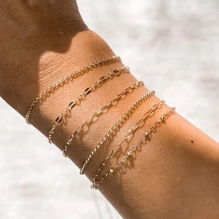 Permanent Jewellery in Sydney: Multiple gold bracelets with different chain styles worn on a person's wrist.