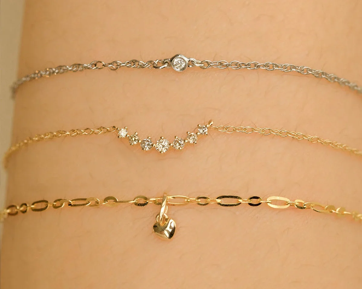 Permanent Jewellery in Sydney: Three layered chain bracelets with different designs, including a heart charm, worn on a wrist.