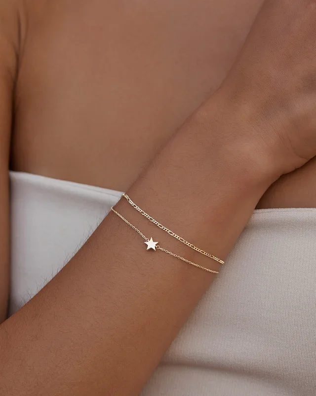 Permanent Jewellery in Sydney: A person's arm decorated with a gold star-shaped bracelet and two thin gold chains, resting against their side or chest, with a white garment in the background.