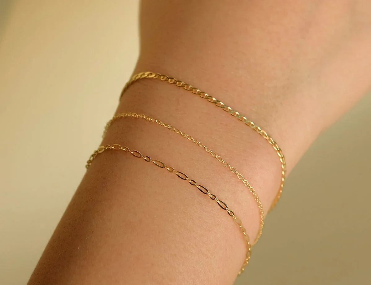 Permanent Jewellery in Sydney:Three gold bracelets on a person's wrist with a plain background.