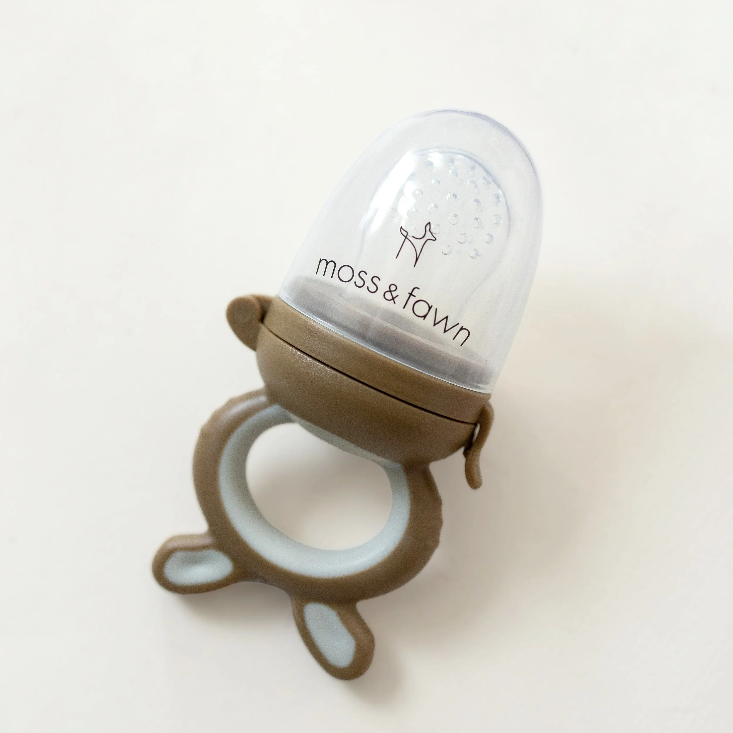 Overhead shot of Moss & Fawn silicone baby feeding set including a bear teether on a solid background.