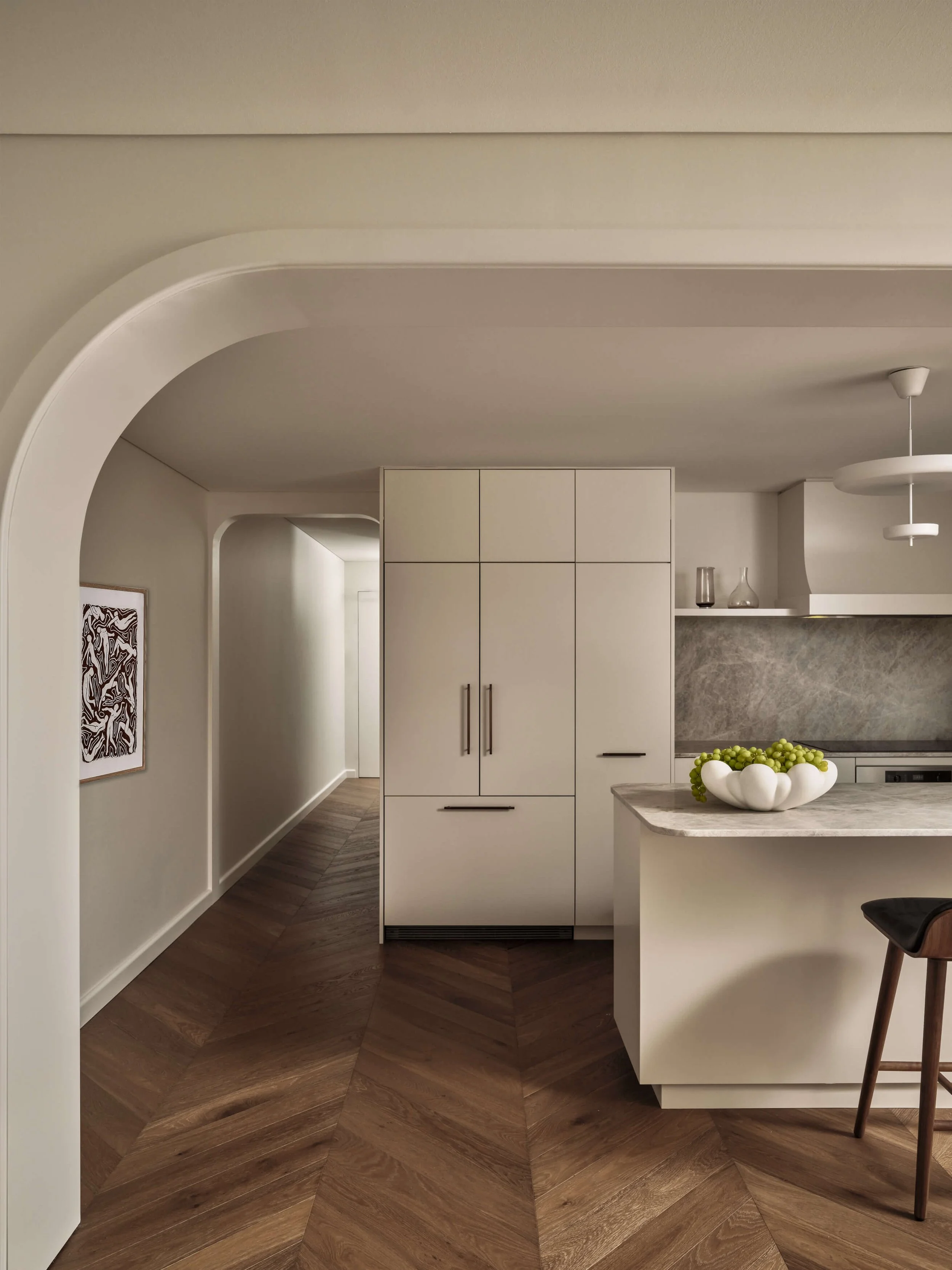 Modern kitchen with white cabinets, marble countertops, and a bowl of green grapes on the island. Wooden flooring and minimal decor.