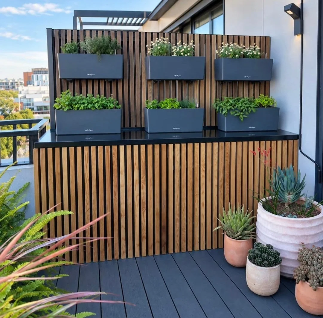 Small garden design on a balcony with timber slats covering an aircon unit, terracotta pots with succulents and native plants