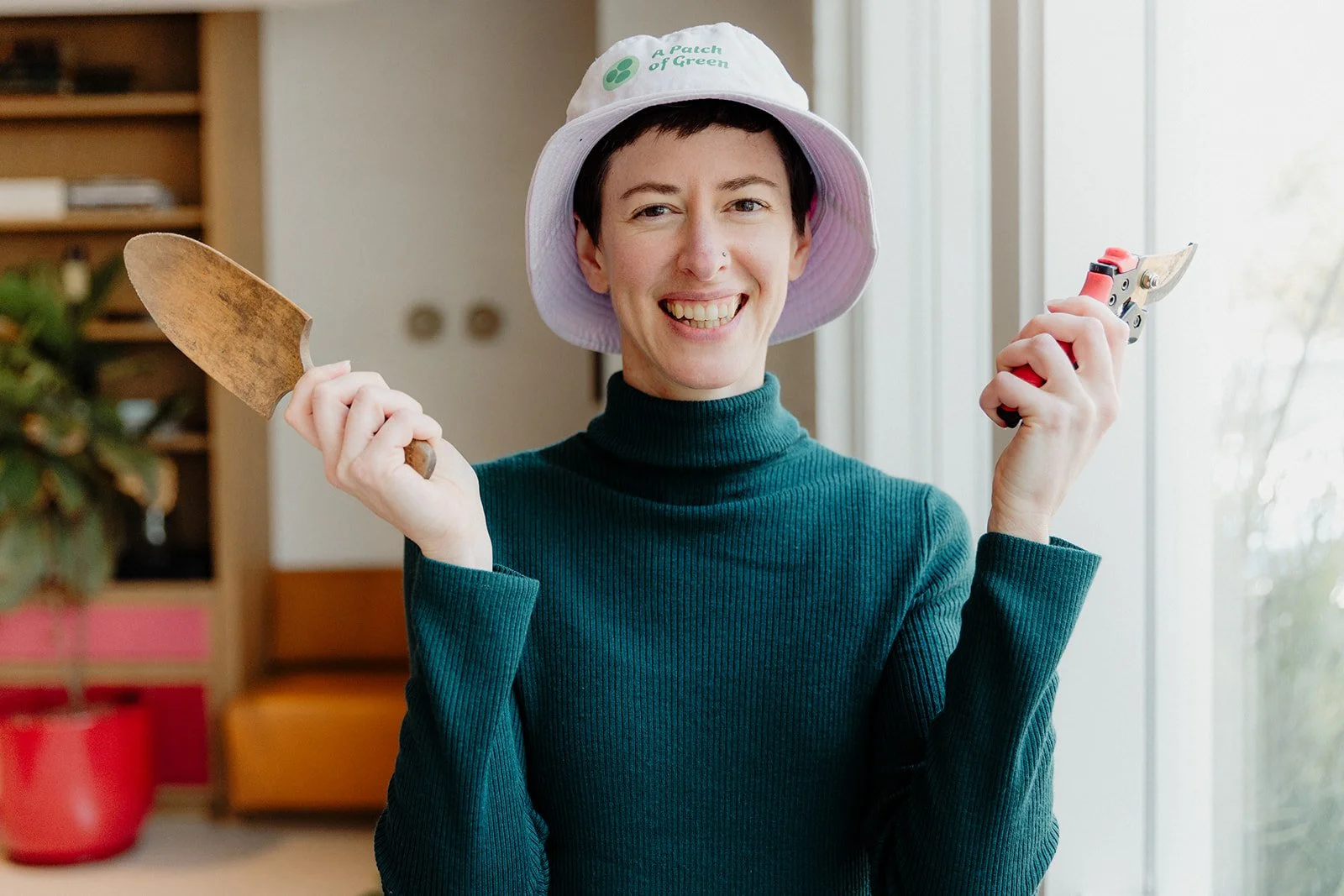 A woman smiling and holding gardening tools