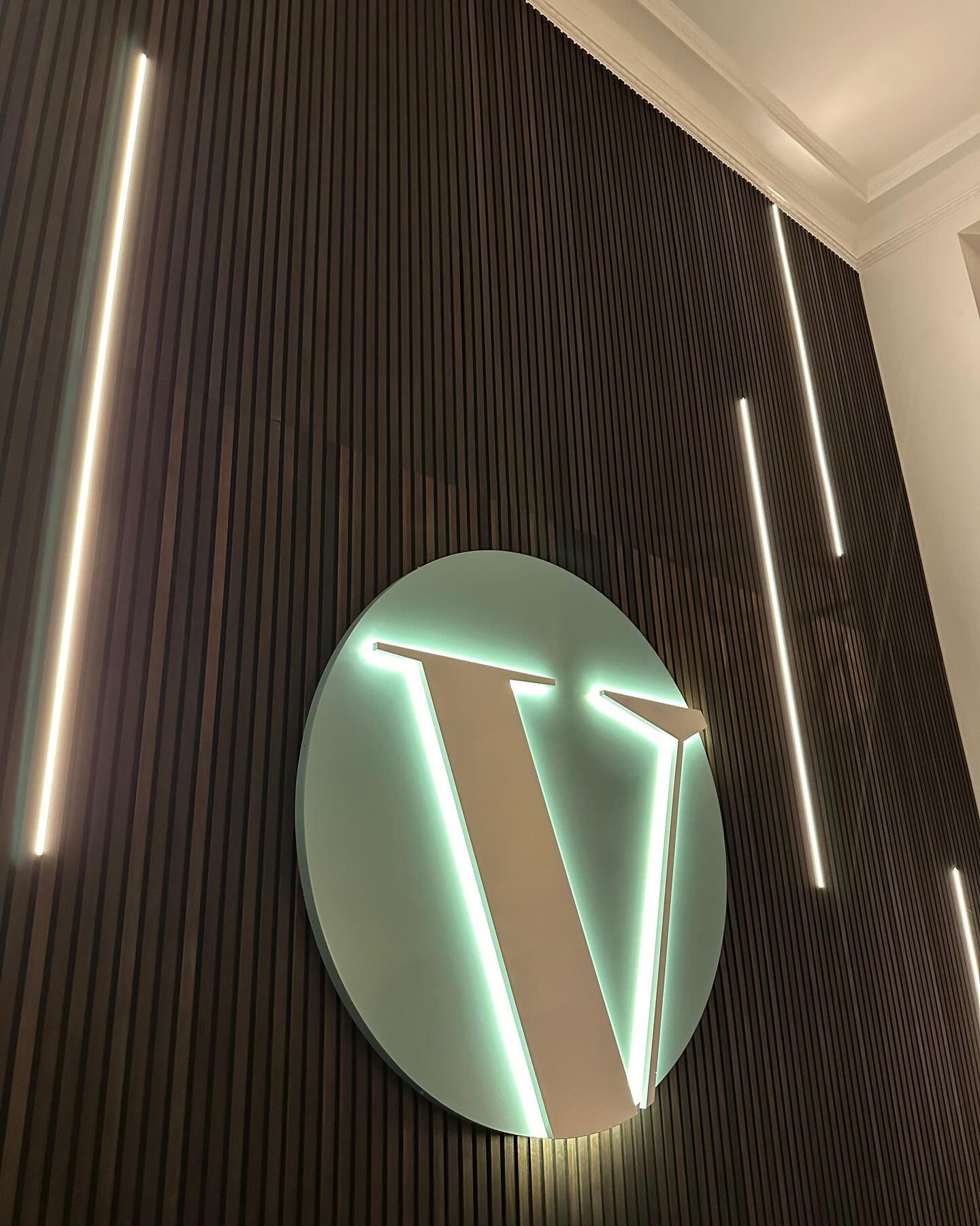 Hinterleuchtetes Logo an dunkler Lamellenwand mit Lichtleisten, Nahaufnahme