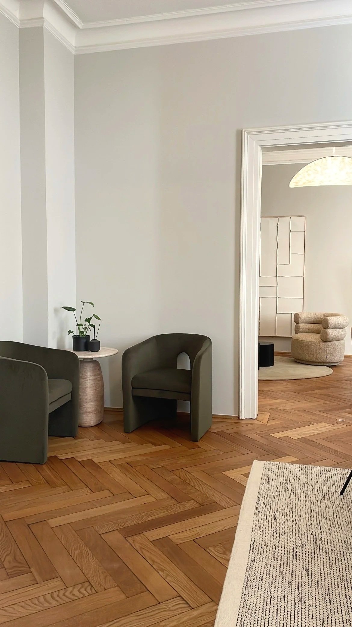 Zwei olivgrüne Polstersessel mit rundem Beistelltisch und Zimmerpflanzen in einem hellen Altbau.