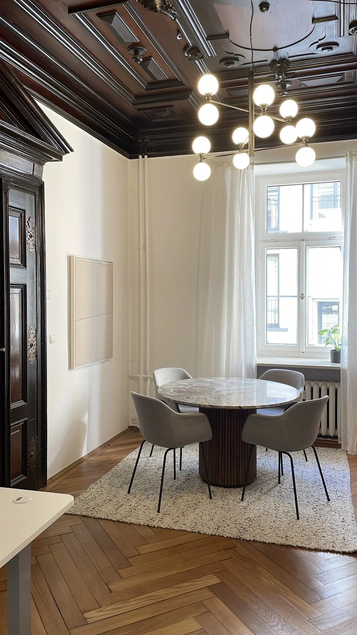 Eleganter Besprechungsraum im Altbau mit dunkler Kassettendecke, rundem Esstisch und Fischgrätparkett.