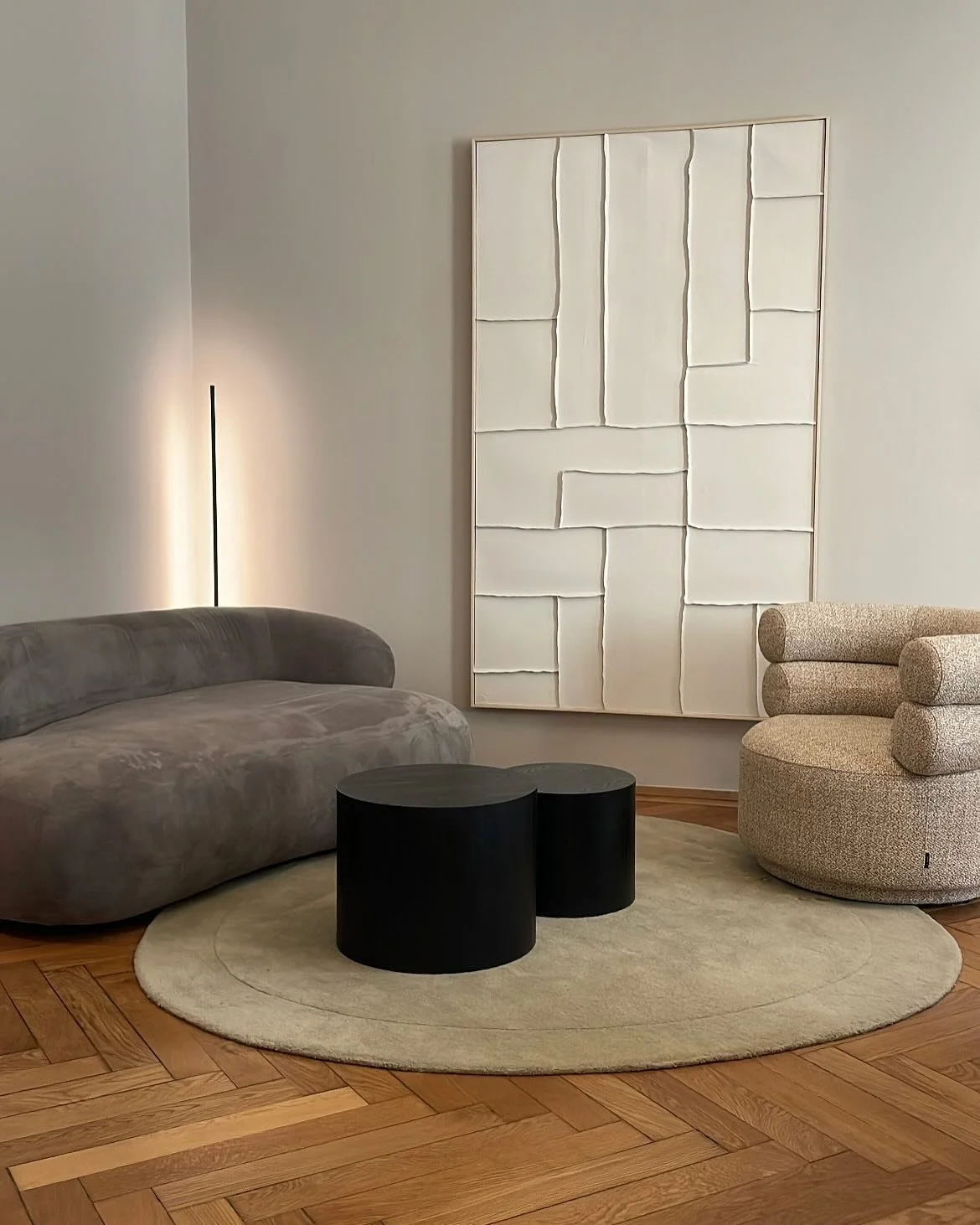 Lounge im Altbau mit geschwungenem Sofa, beigefarbenen Sesseln, abstraktem Wandbild und großer Pendelleuchte.