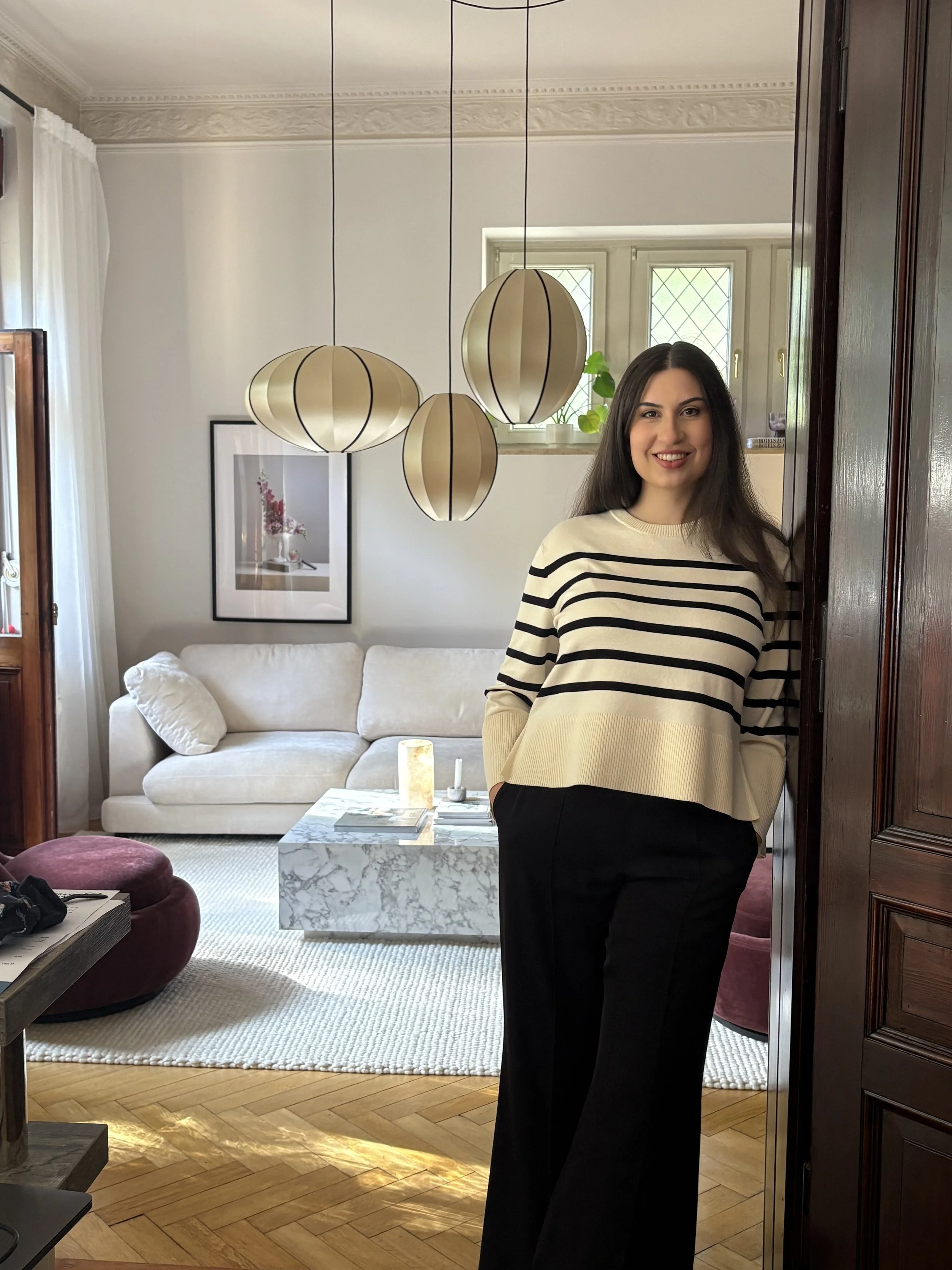 Maria Levich, Interior Designerin aus Dresden, in gestreiftem Oberteil in einem von ihr gestalteten Wohnzimmer mit weißem Sofa, Marmor-Couchtisch und Wandbild.