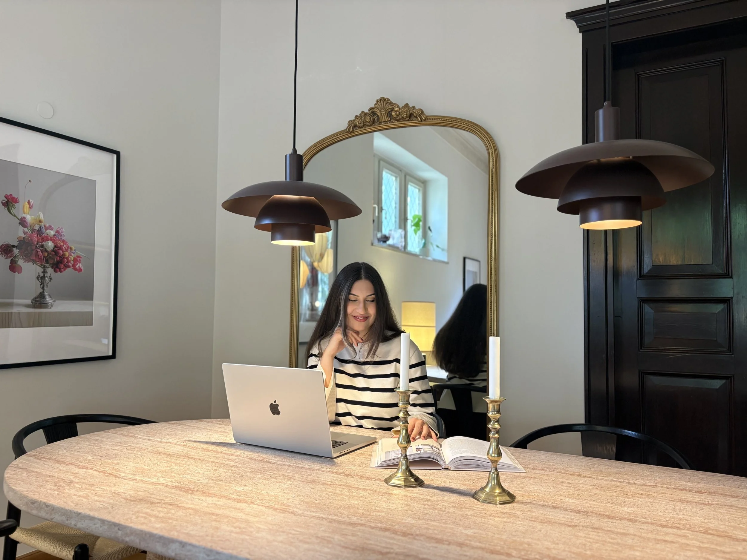 Maria Levich, Interior Designerin aus Dresden, sitzt an einem runden Esstisch mit Laptop in einem von ihr gestalteten, stilvoll beleuchteten Wohnbereich.