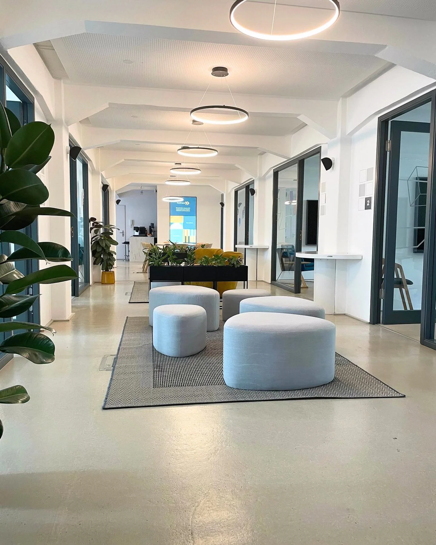 Fertiger Bürokorridor mit Sitzpoufs und Ring-Pendelleuchten