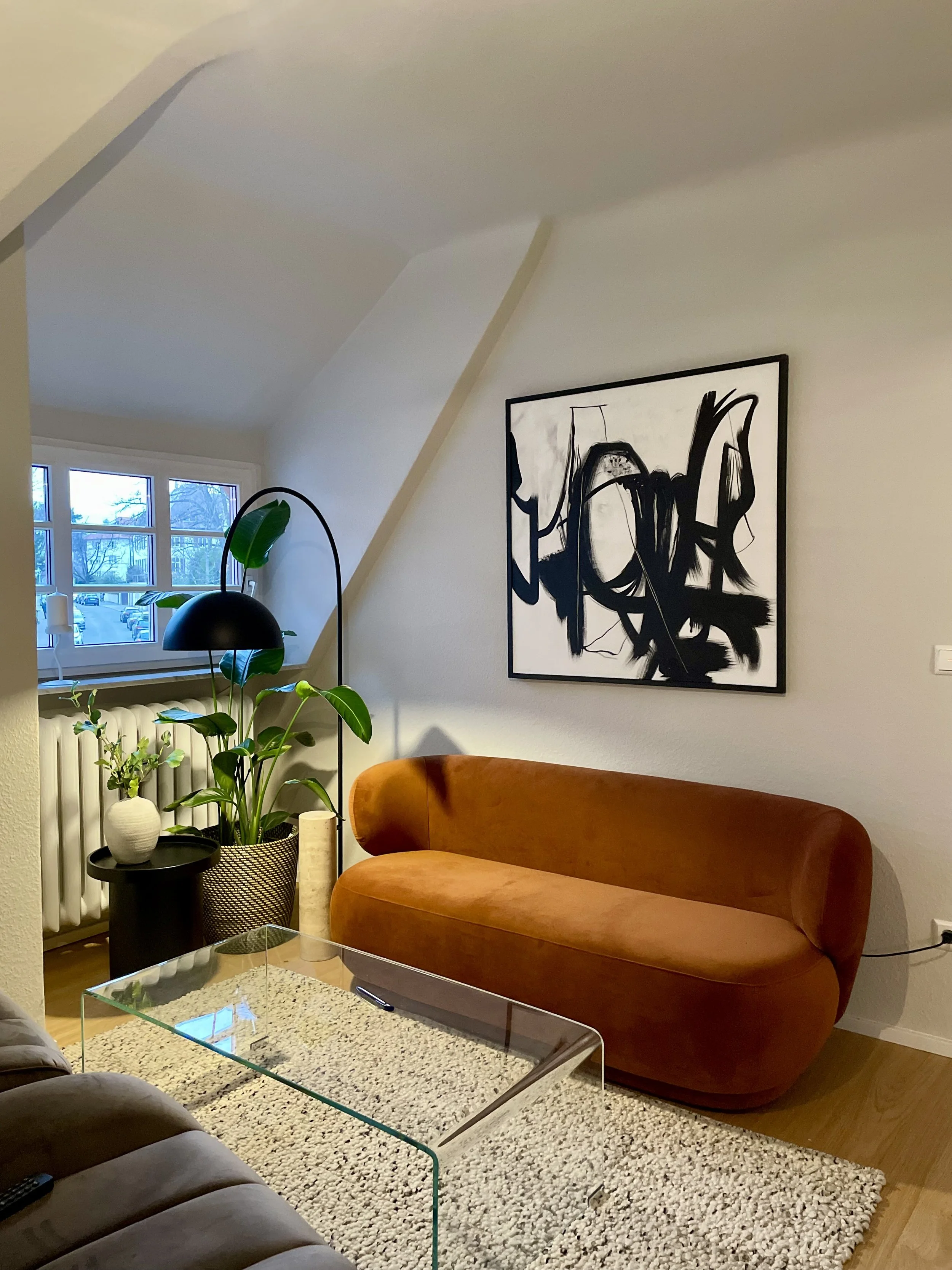 Modernes Interior Design eines Empfangsbereiches mit rostfarbenem Samtsofa, abstrakter Wandkunst, Glas-Couchtisch und grünen Zimmerpflanzen – individuelle Innenarchitektur von MARIA LEVICH.