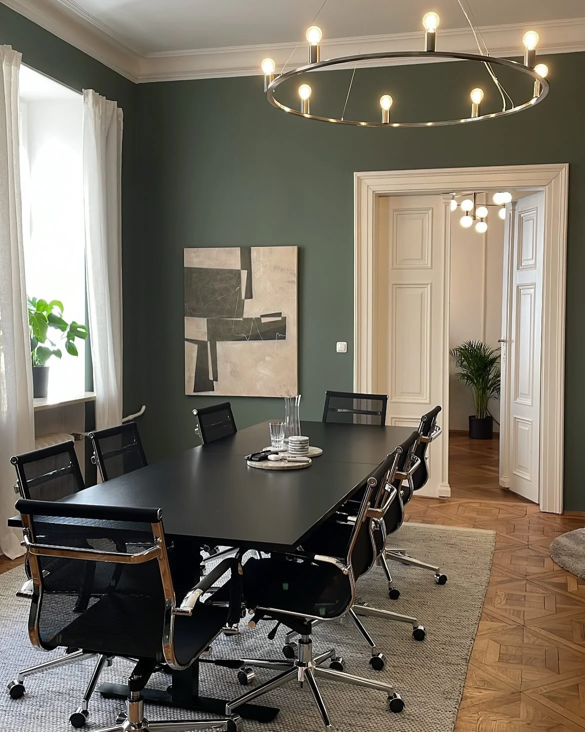 Besprechungsraum im Altbau mit schwarzem Konferenztisch, Drehstühlen und dunkelgrüner Wand.
