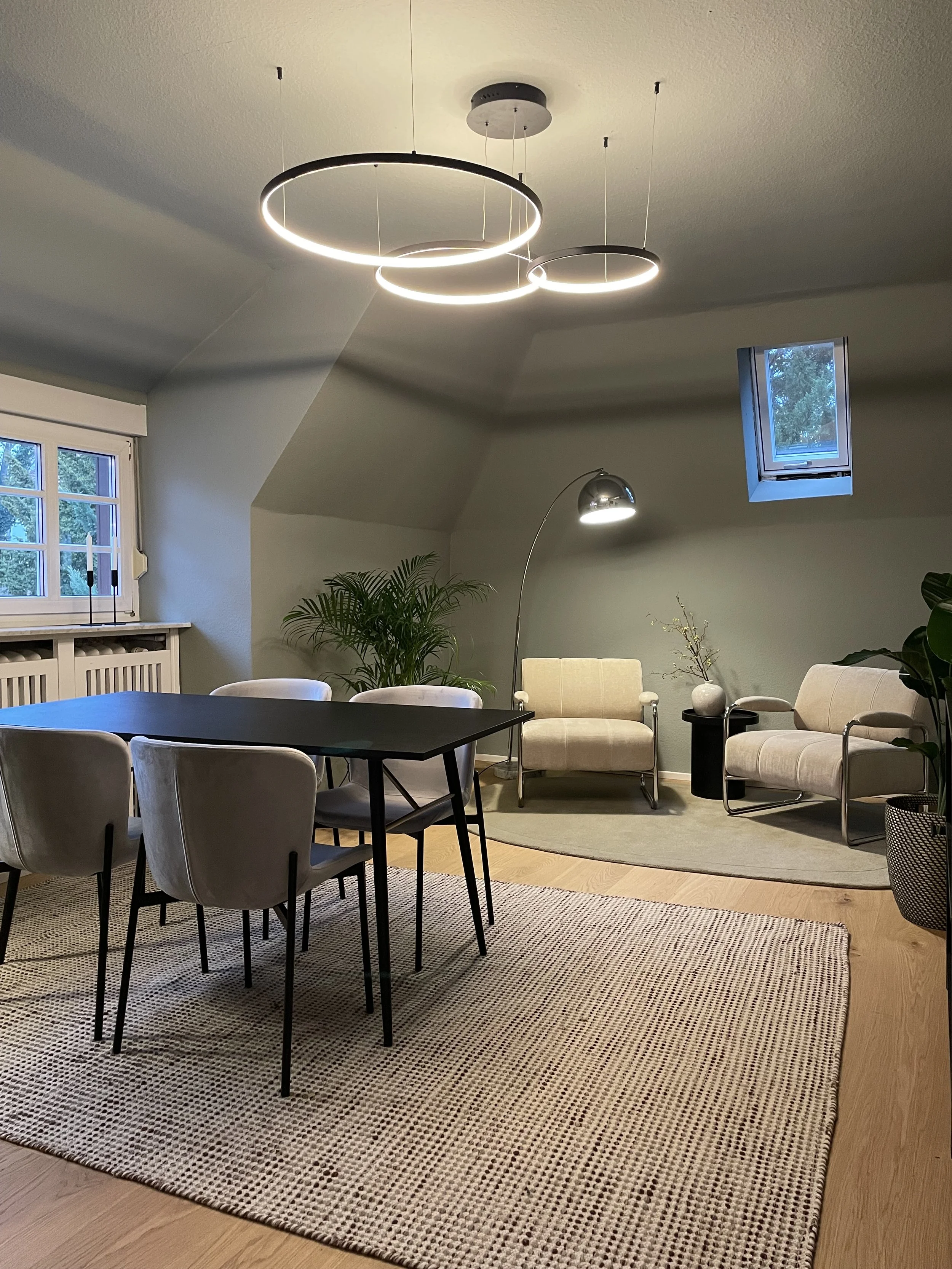 Modern gestalteter Büroraum mit Besprechungstisch, hellen Polsterstühlen, eleganten Ringpendelleuchten und gemütlicher Sitzecke – Interior Design von MARIA LEVICH.