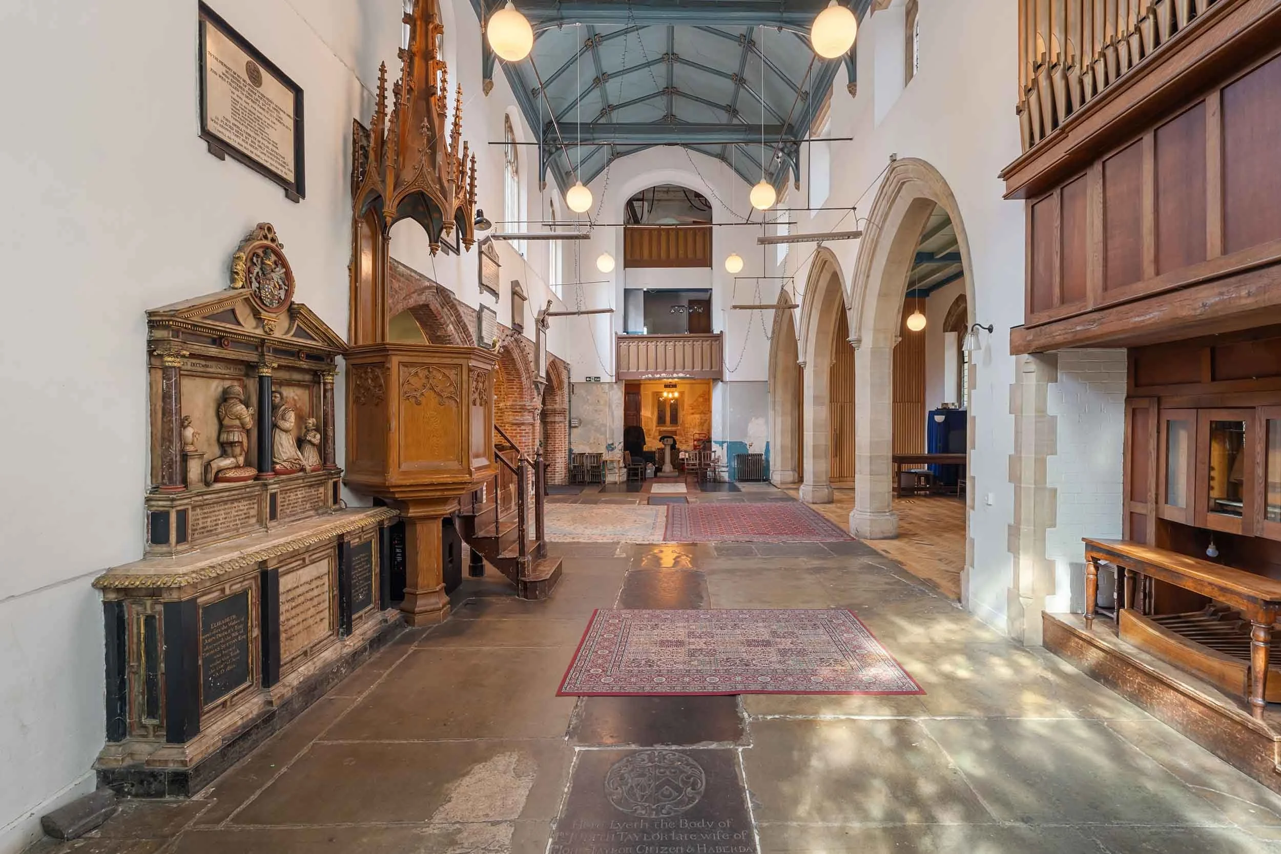 Wide nave with stone arches, rugs on the floor, stained-glass windows, and hanging globe lights.