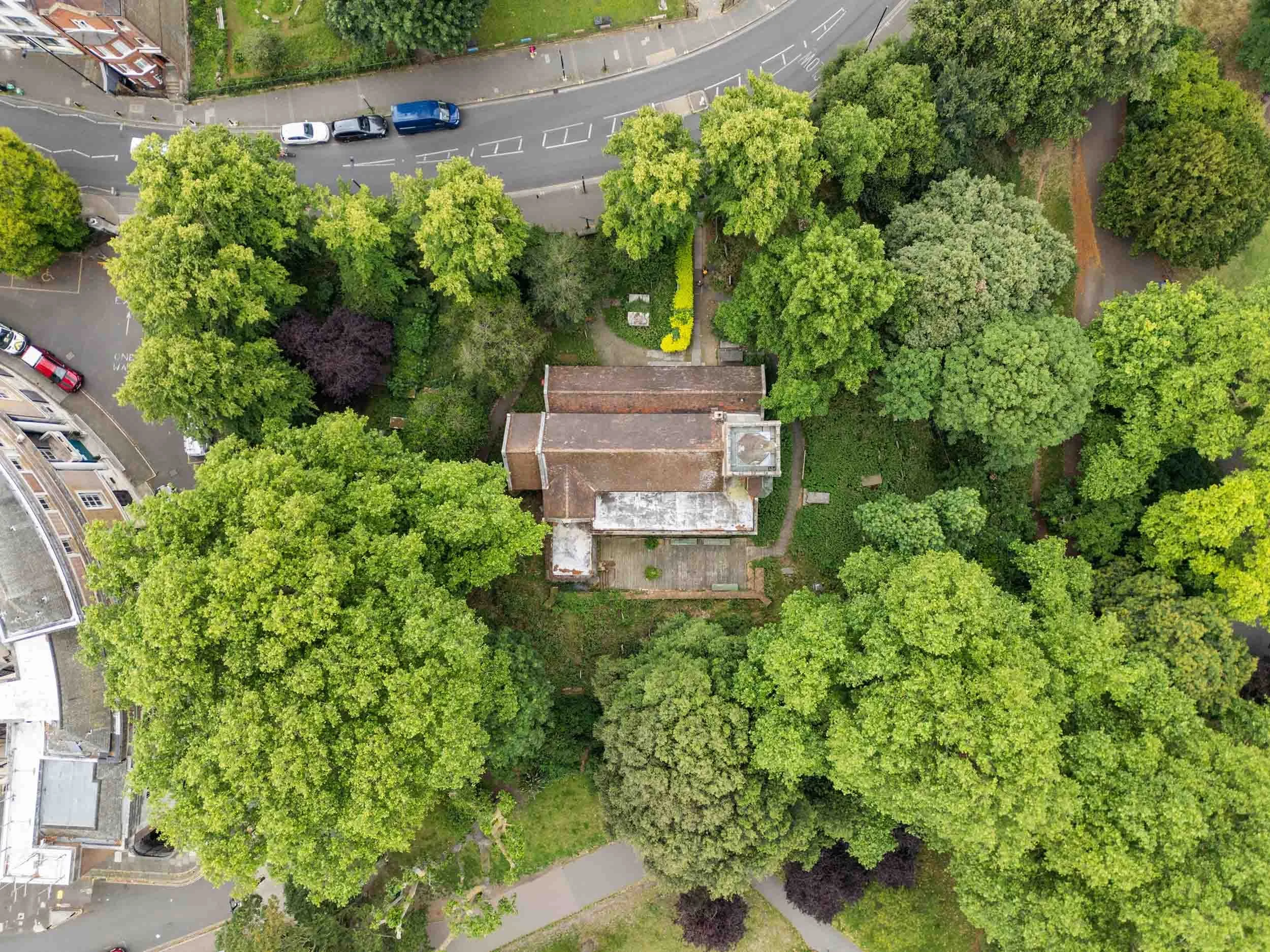 Brick church exterior with arched windows and a tall spire rising above the roofline, framed by trees.