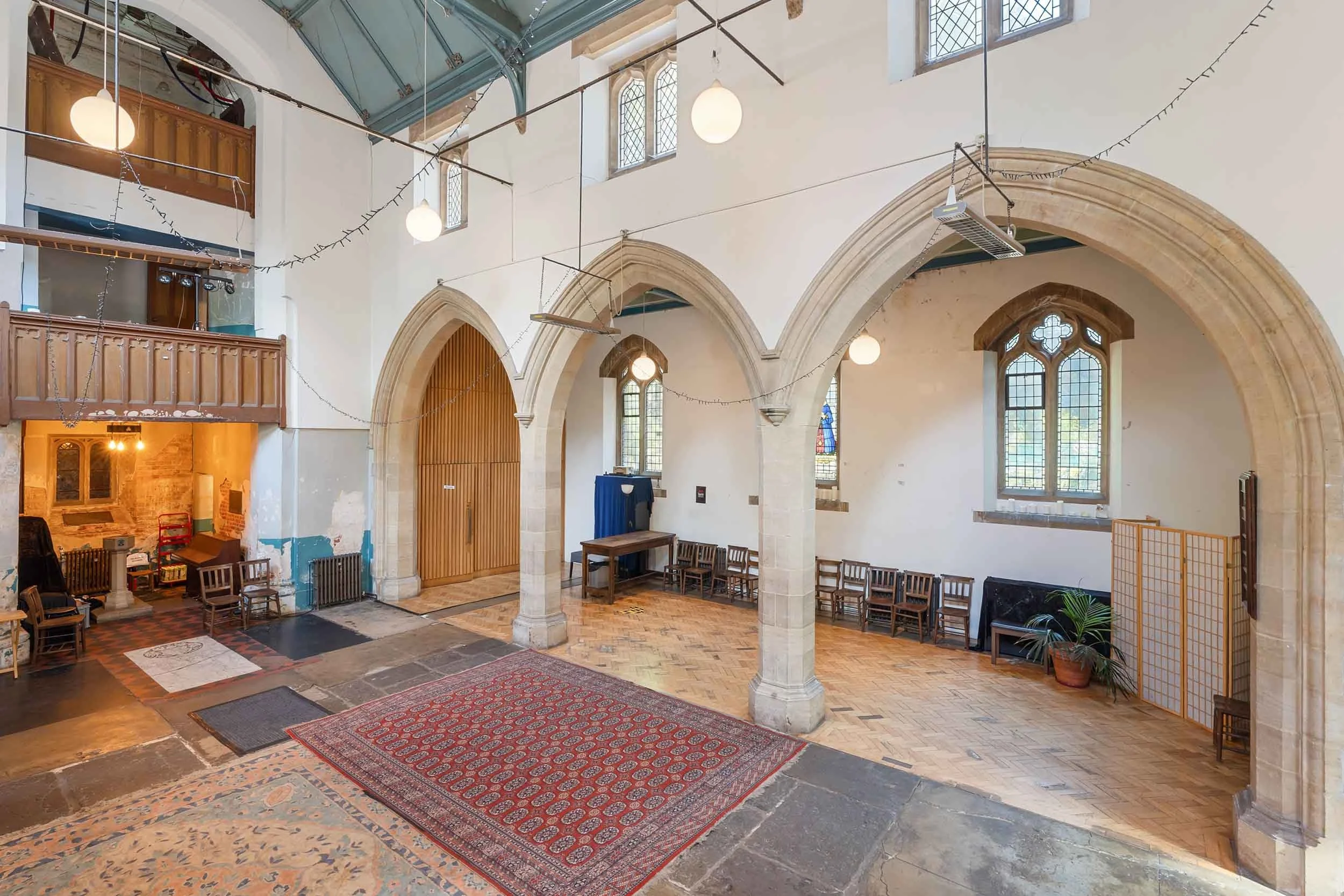 Long interior view with memorial plaques, carved wooden pulpit, brick arches, and patterned rugs on a stone floor.