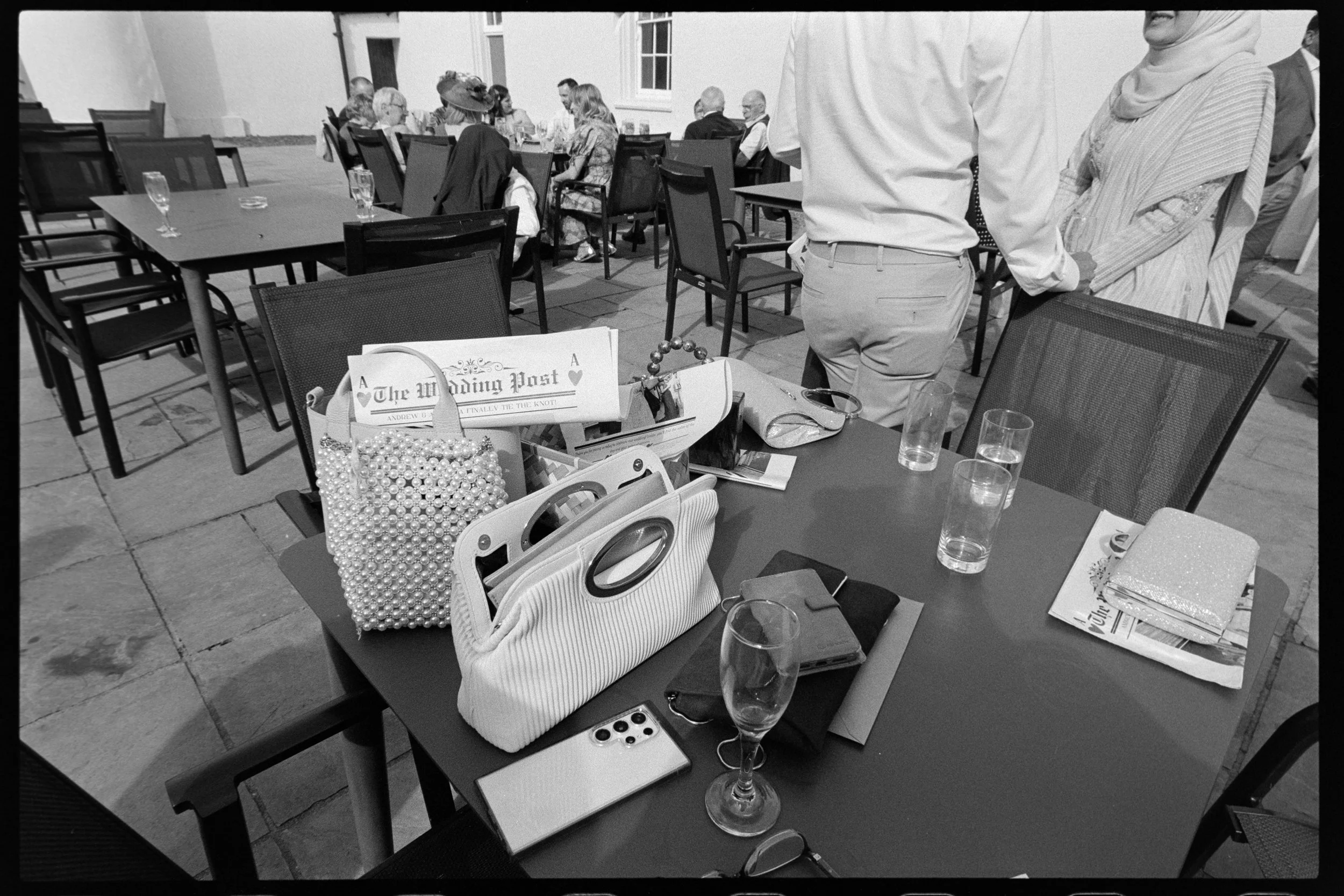 Documentary wedding flatlay of a table with handbags, empty glasses and a wedding newspaper
