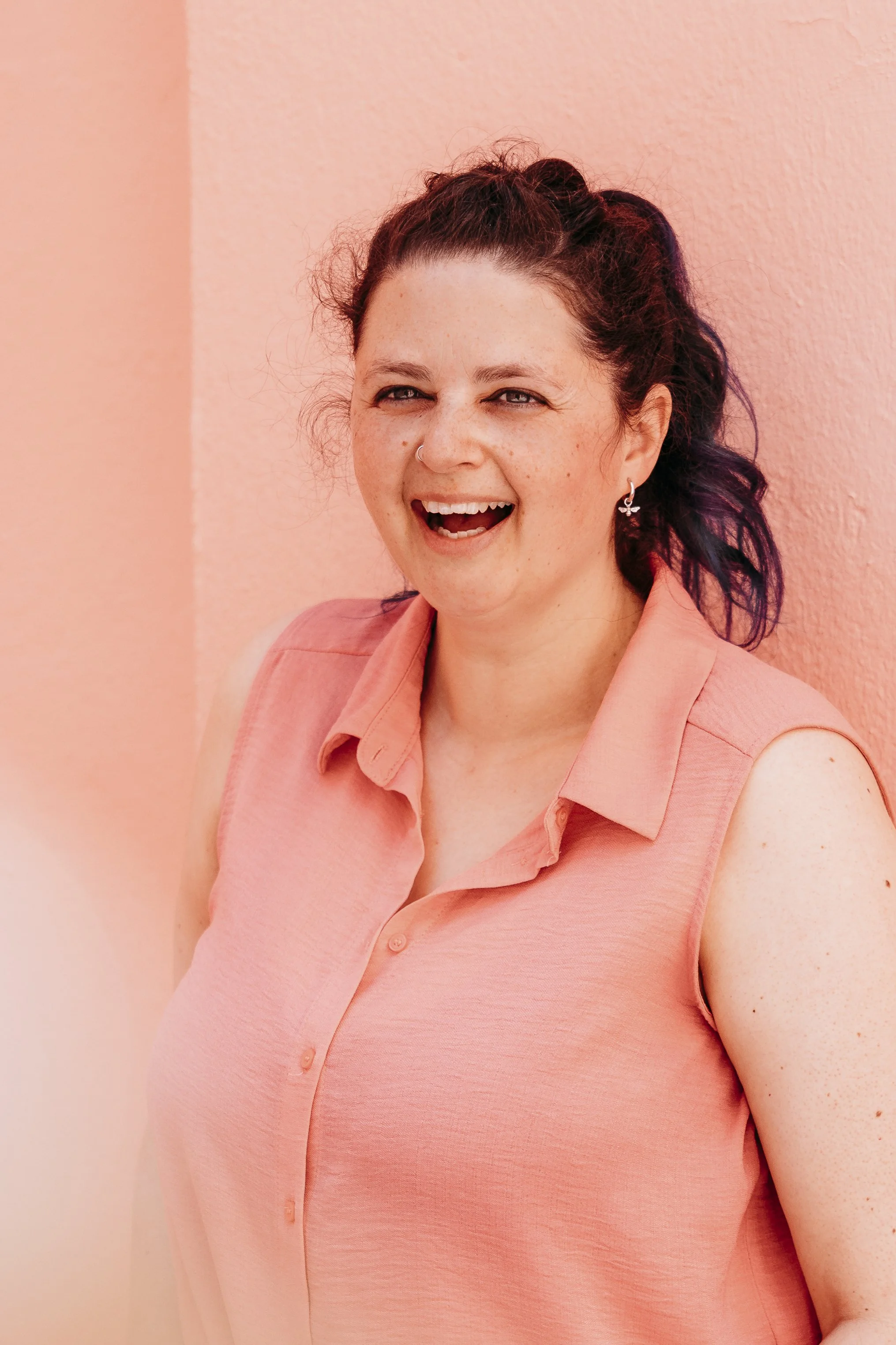 smiling woman wearing a pink shirt, against a peach background