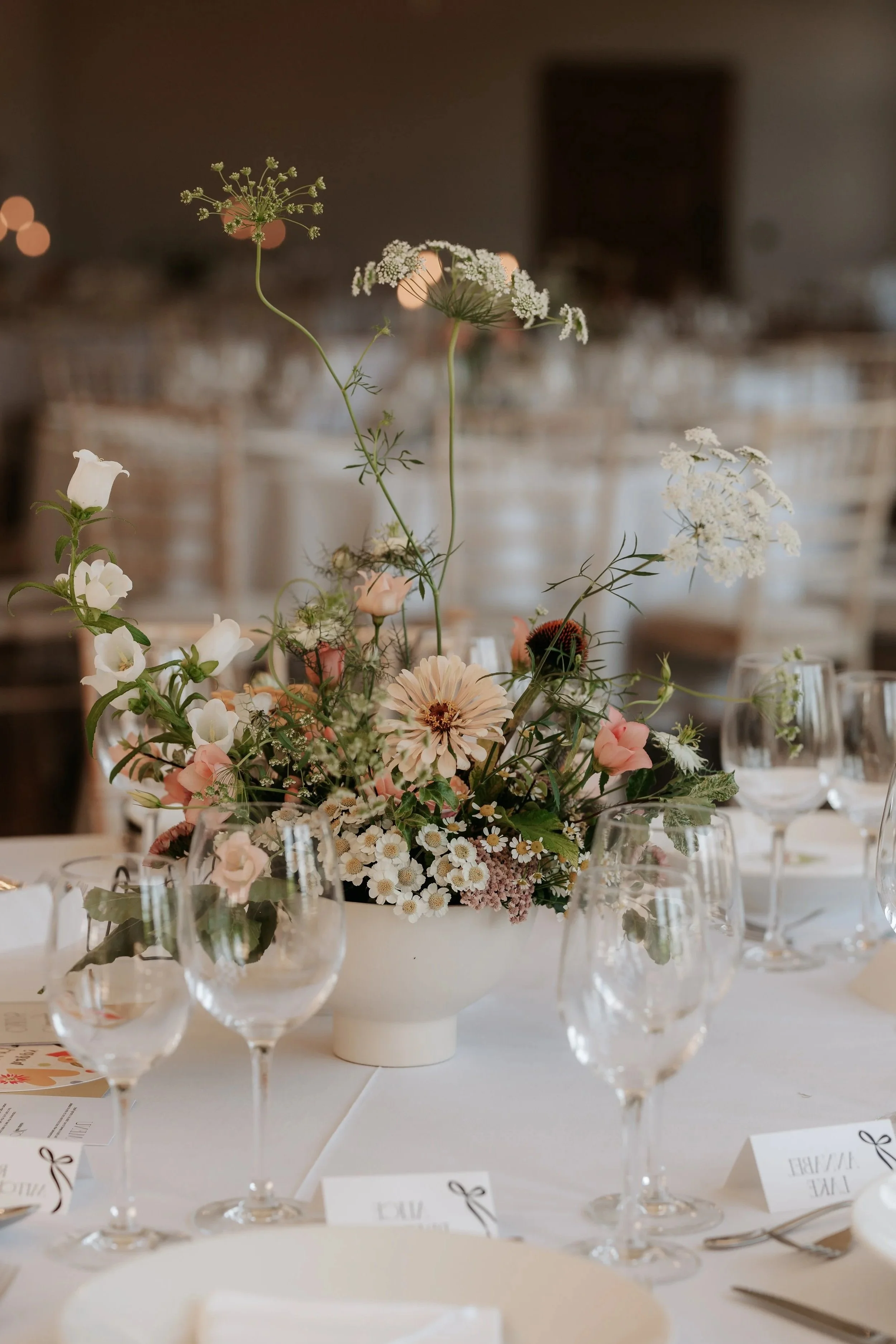 Elegant table centerpiece with white and pink flowers, surrounded by wine glasses on a formal event table.