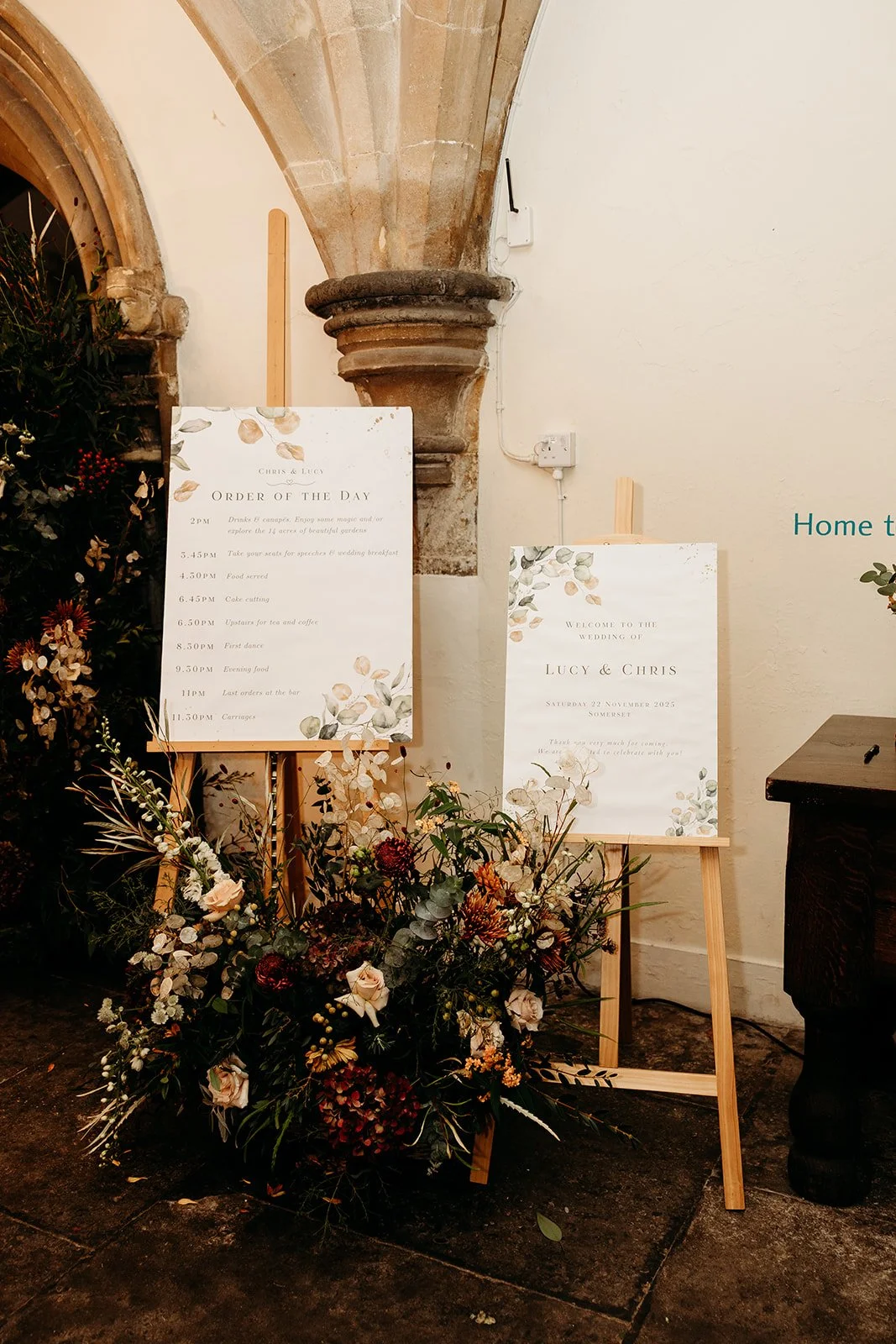 Wedding welcome sign for Lucy and Chris with schedule and floral decorations, set in an indoor venue with stone architecture.
