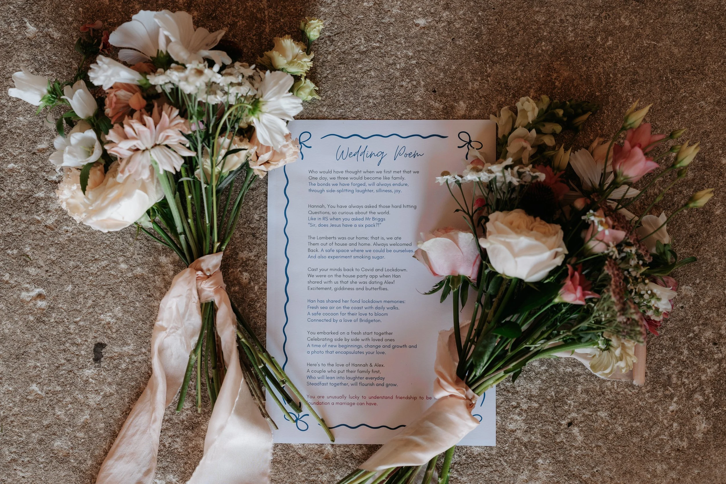 Wedding poem printed on white paper, surrounded by pink and white flowers with satin ribbons, on a textured brown surface.
