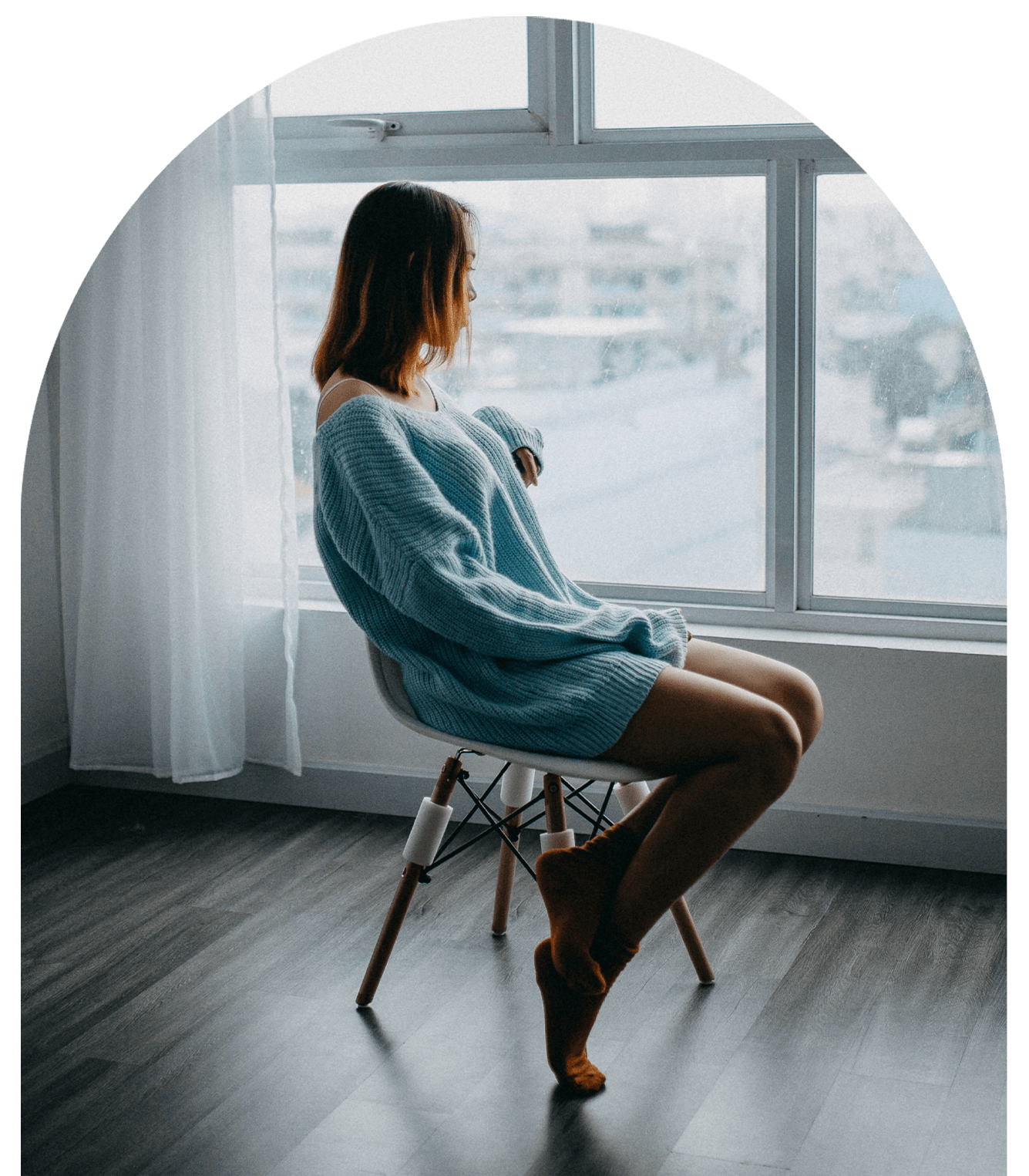 Woman in a blue sweater sitting by a window, feeling anxious and overwhelmed