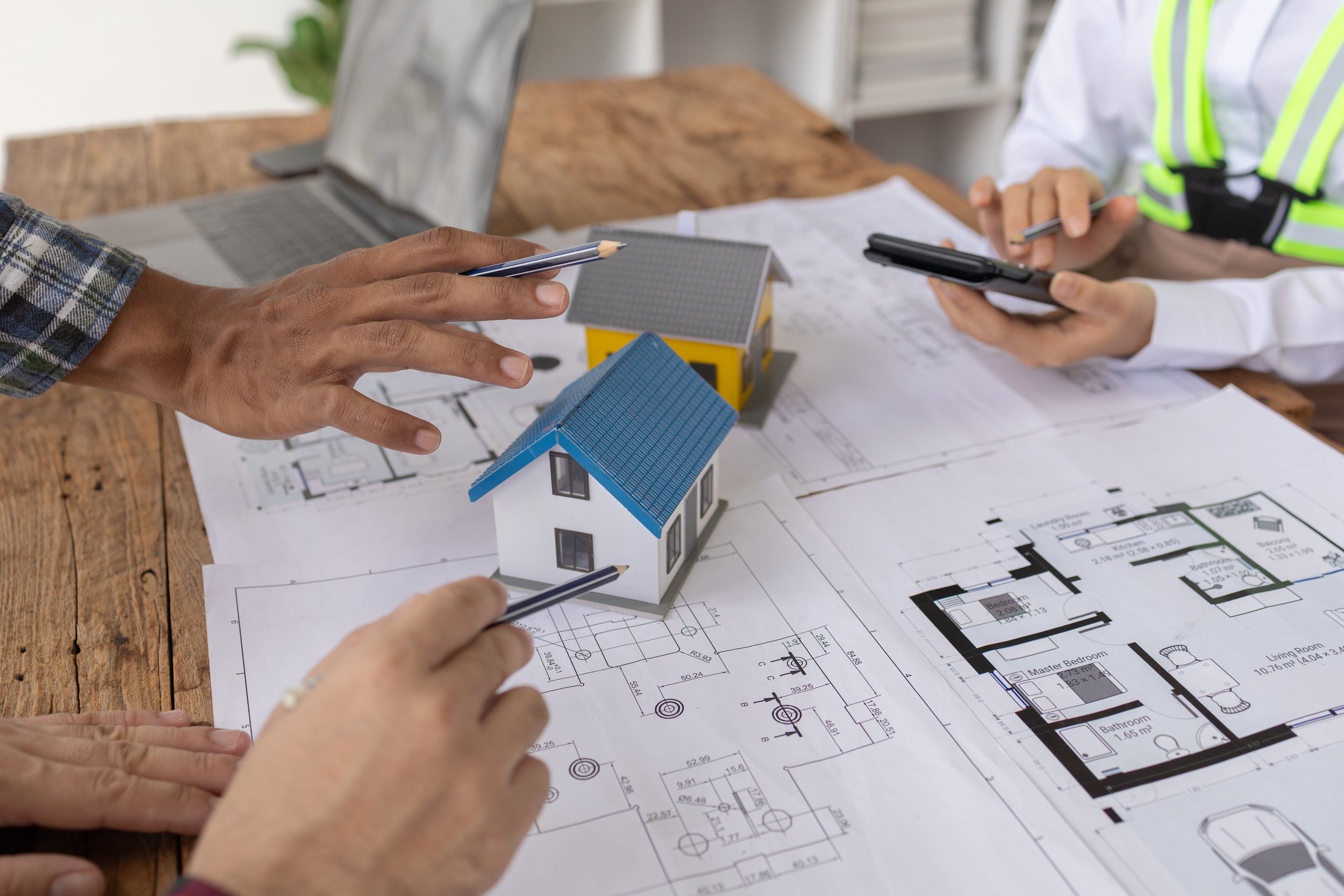 A woman holds a stamp over rolled blueprints on a desk alongside a hard hat and small house model.