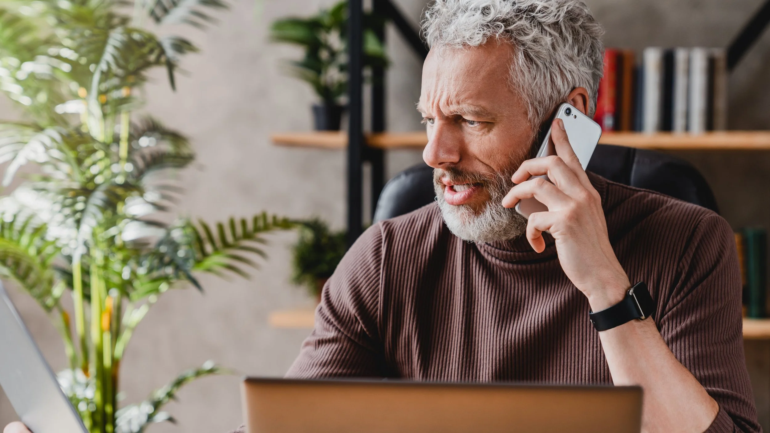 Architect on the phone at his desk with rain visible through the office window
