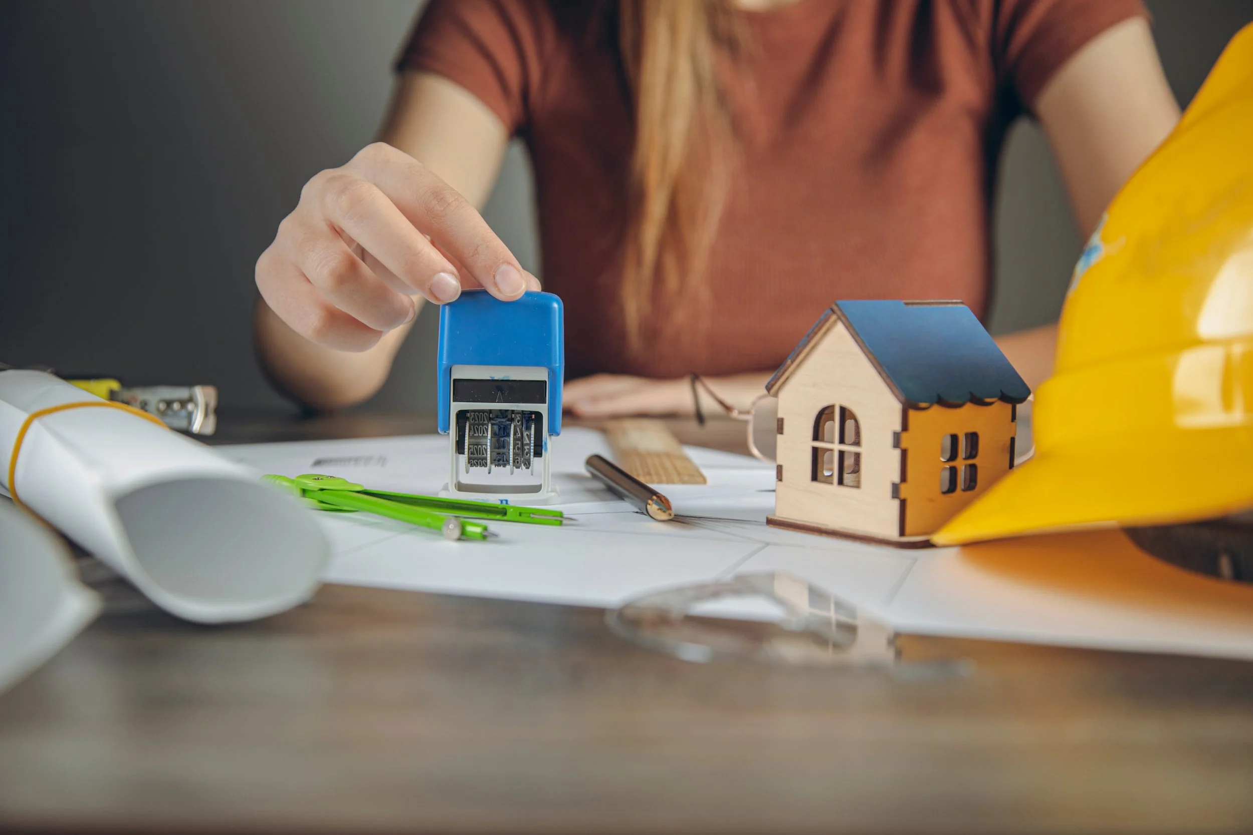 Architects and a construction professional review building blueprints alongside a small house model on a wooden table.