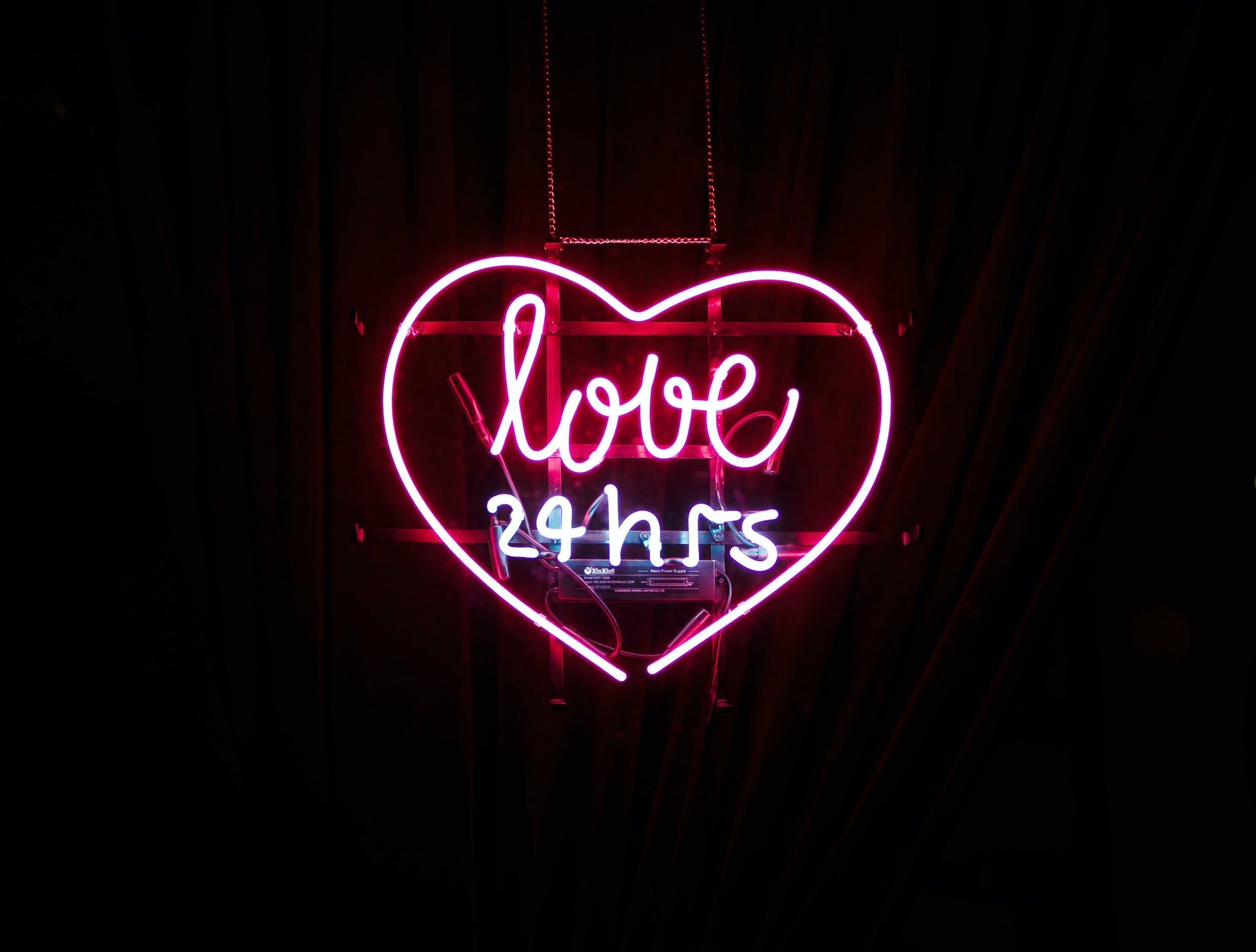 Illuminated neon sign that reads "Love 24 hrs"