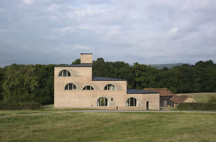 Rectangular brick building with arched windows on several levels with woodland background