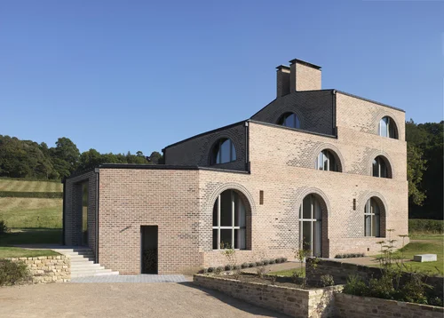 Rectangular brick building with arched windows on several levels with woodland background