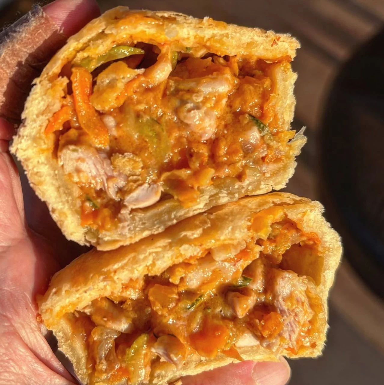 Hand holding a split pastry filled with cooked meat and vegetables